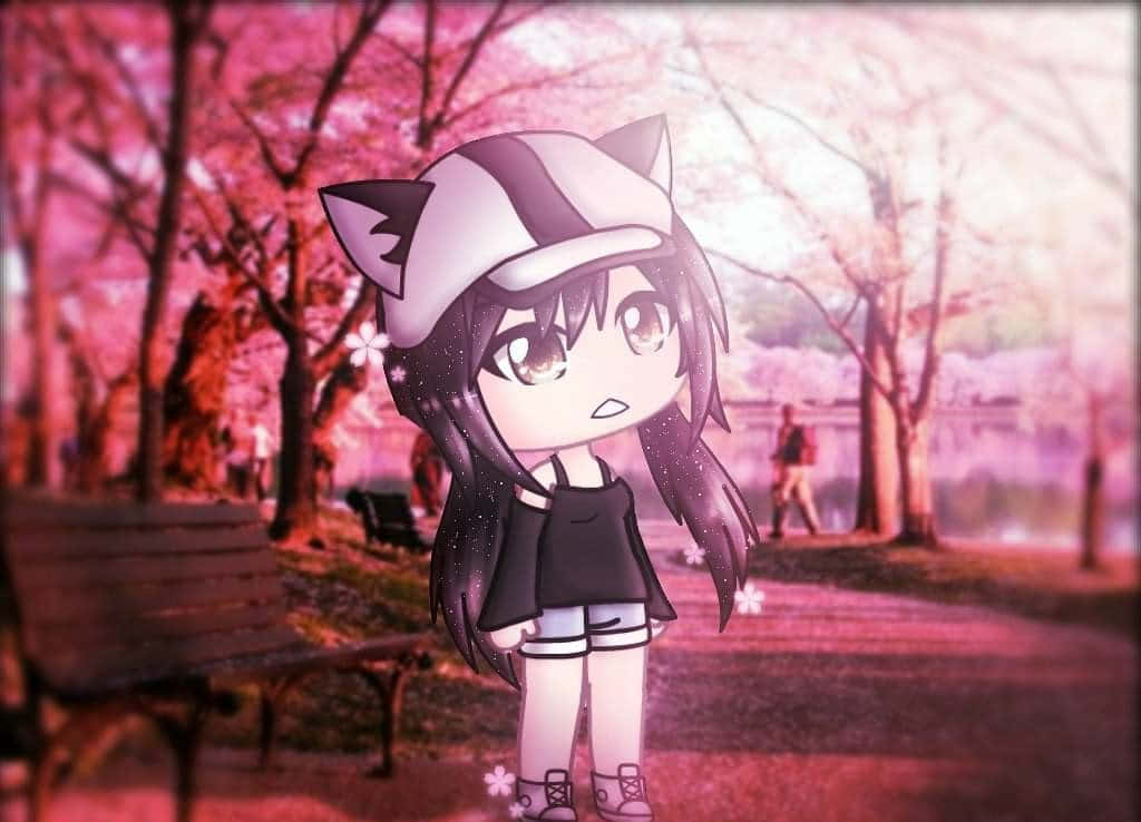 Gacha 桌布 壁紙 — 一個戴著貓耳和帽子的Q版動漫女孩，站在公園裡粉紅色的櫻花下，伴隨著柔和的光芒。