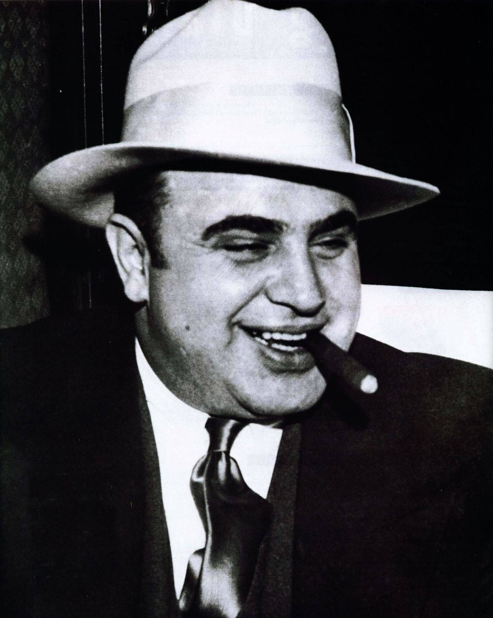 Capone 桌布 壁紙 — 一個戴著軟呢帽和西裝、嘴裡叼著雪茄的微笑男子的黑白肖像。