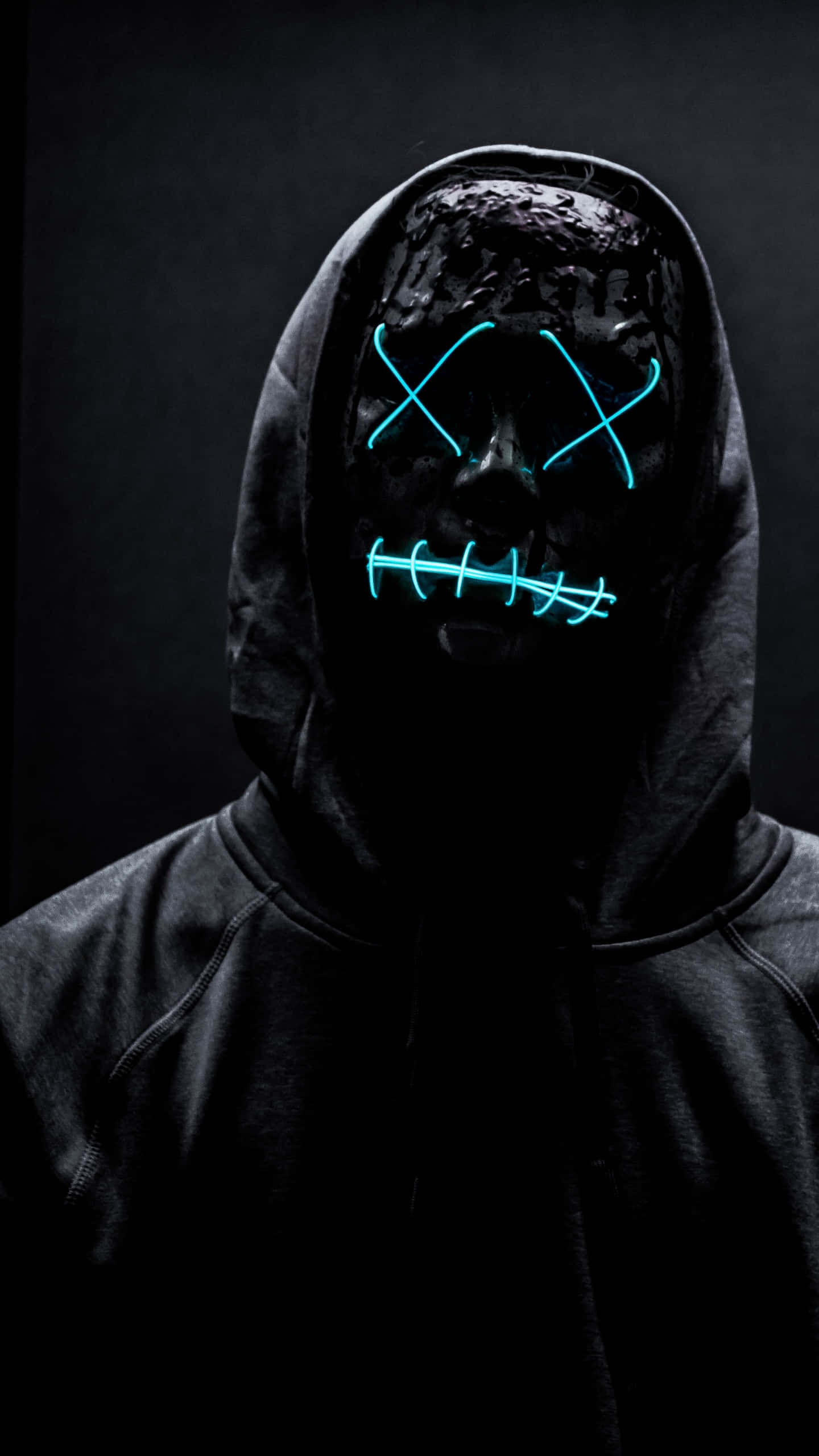 Mask Boy 桌布 壁紙 — 一個戴著連帽的人物，戴著發光的藍色霓虹面具，面具上有縫合的眼睛和嘴巴，背景為黑色。