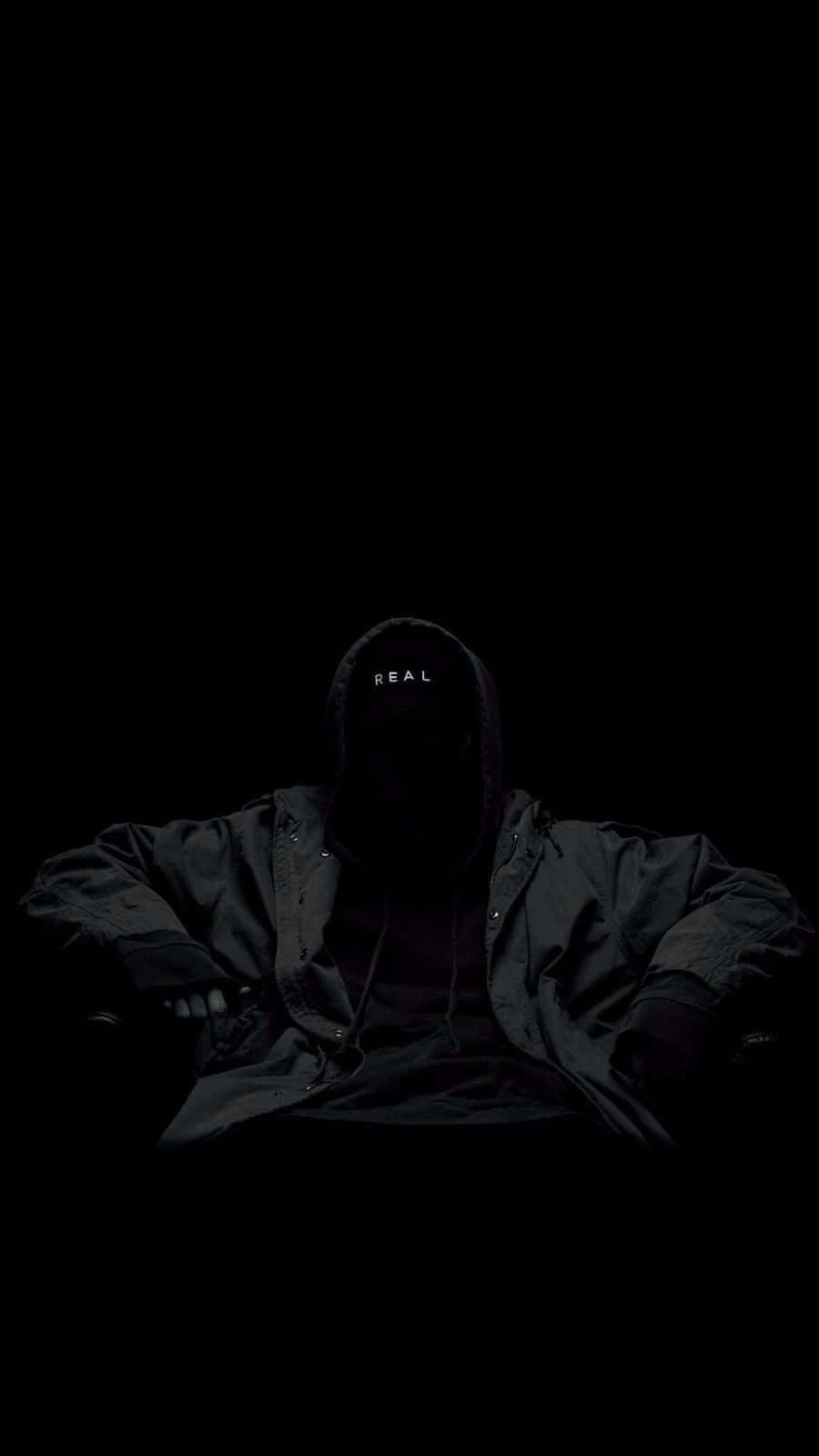 Dark Room 桌布 壁紙 — 一個戴著連帽的人物坐在黑暗中，黑色背景上只有帽子上的「REAL」字樣可見。