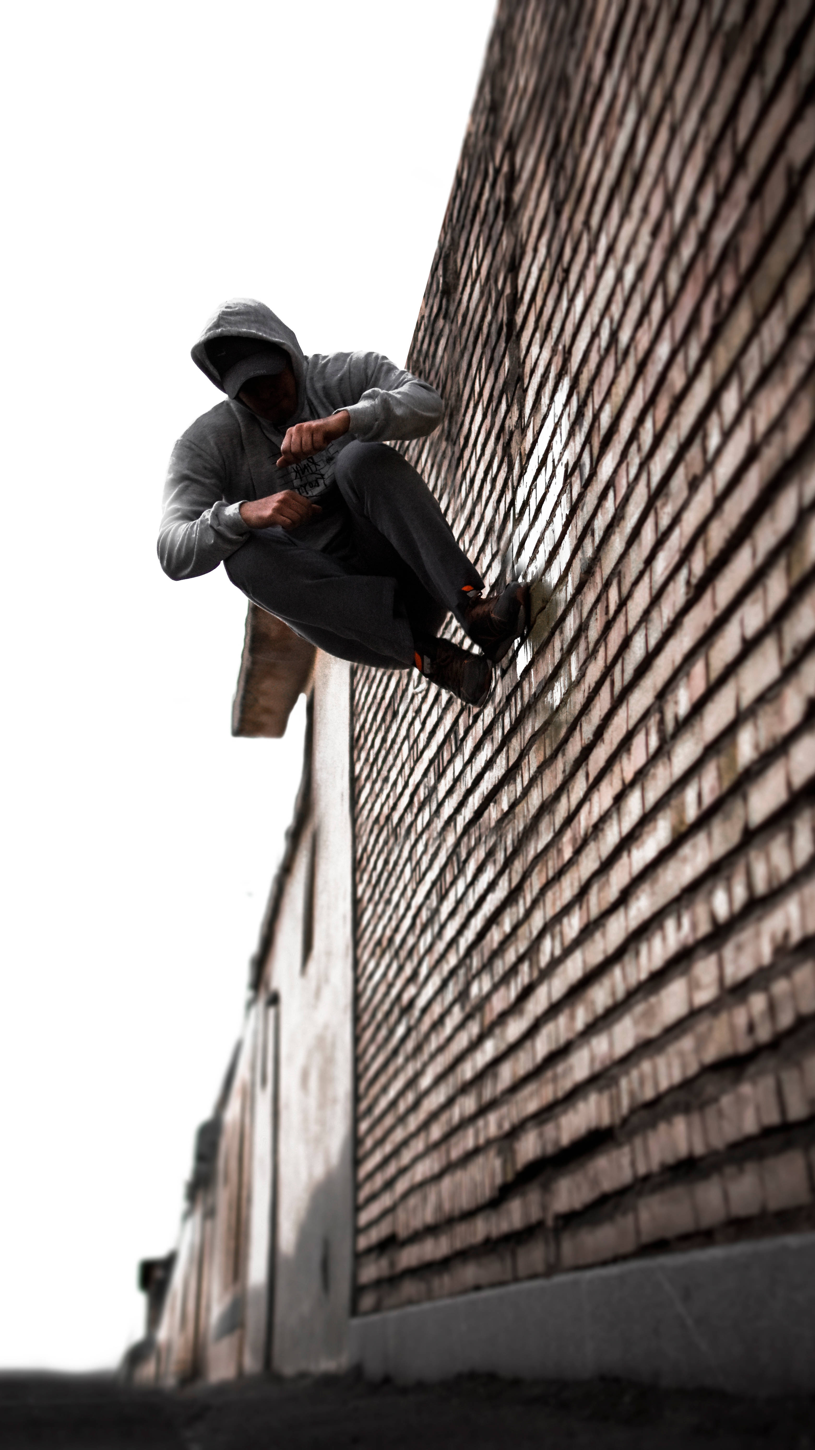 Parkour 桌布 壁紙 — 一個戴著連帽衫的人坐在城市小巷的磚牆上，天空明亮。