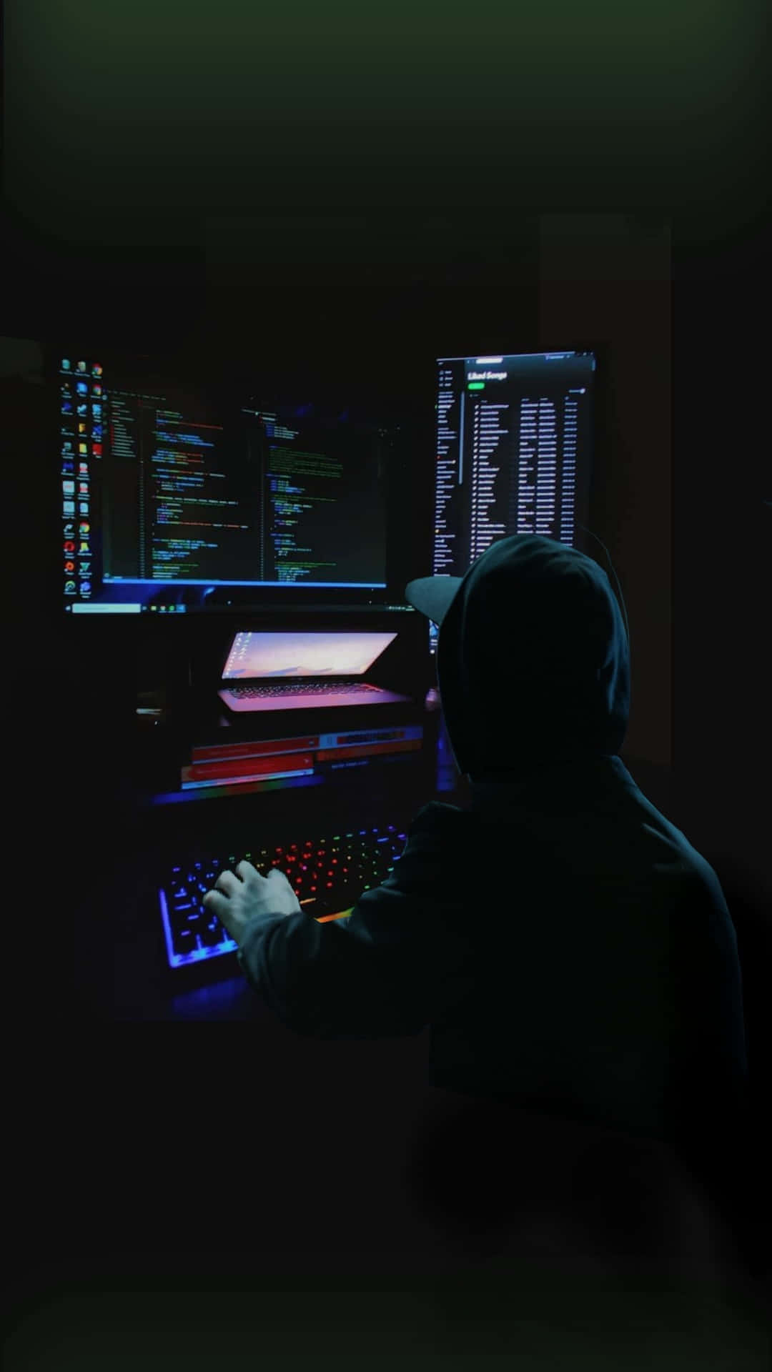 Dark Room 桌布 壁紙 — 一個戴著連帽衫的人物在黑暗的房間裡，在發光的鍵盤上打字，周圍環繞著多個顯示程式碼和資料的顯示器。