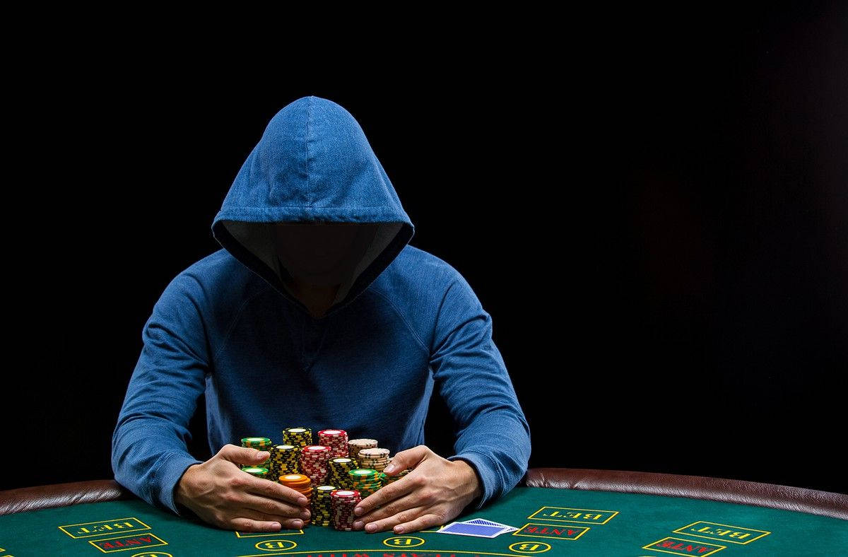 Man 桌布 壁紙 — 一個戴著連帽衫的人物坐在賭桌旁，周圍是籌碼，燈光效果戲劇化。
