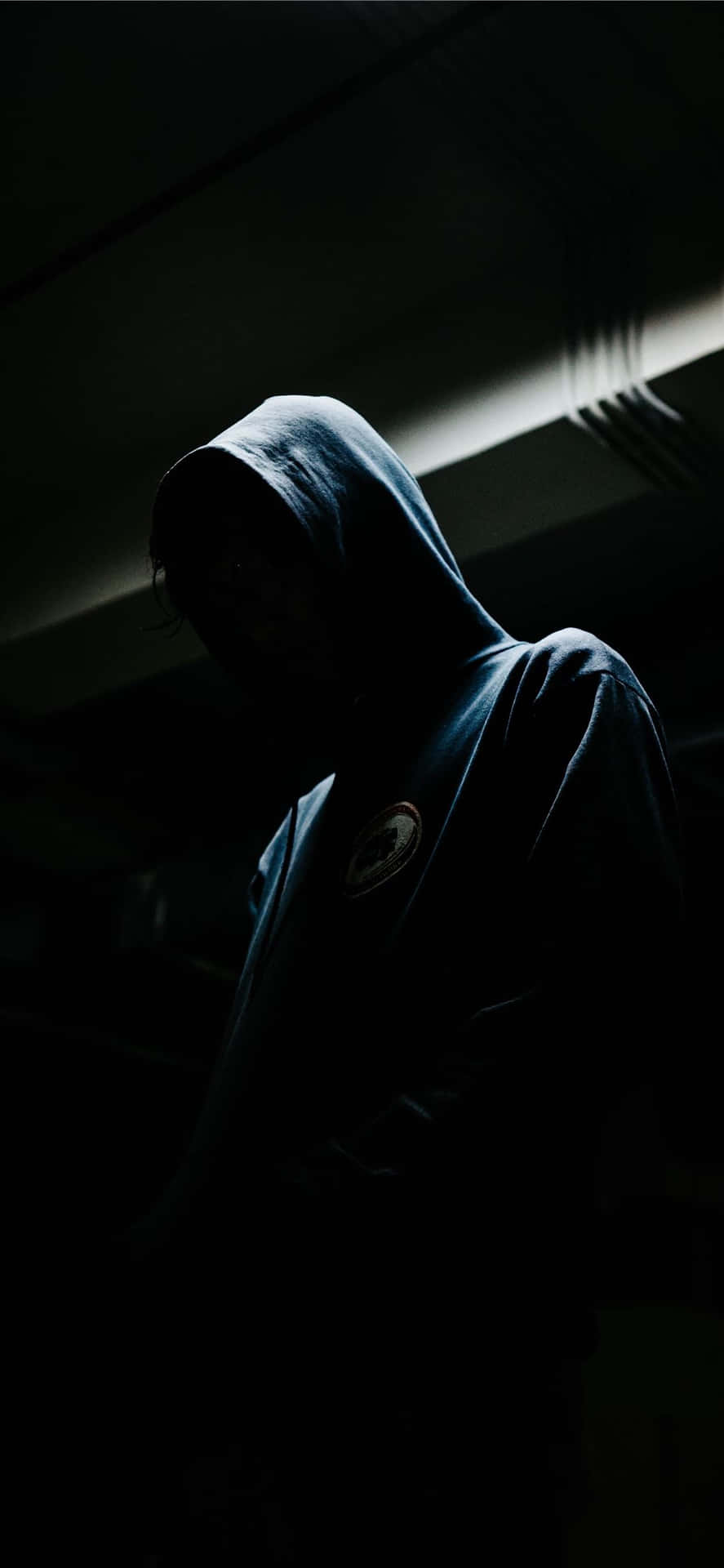 一個穿著深色連帽衫的人站在陰影中，光線極少。 — 憂鬱男孩 壁紙