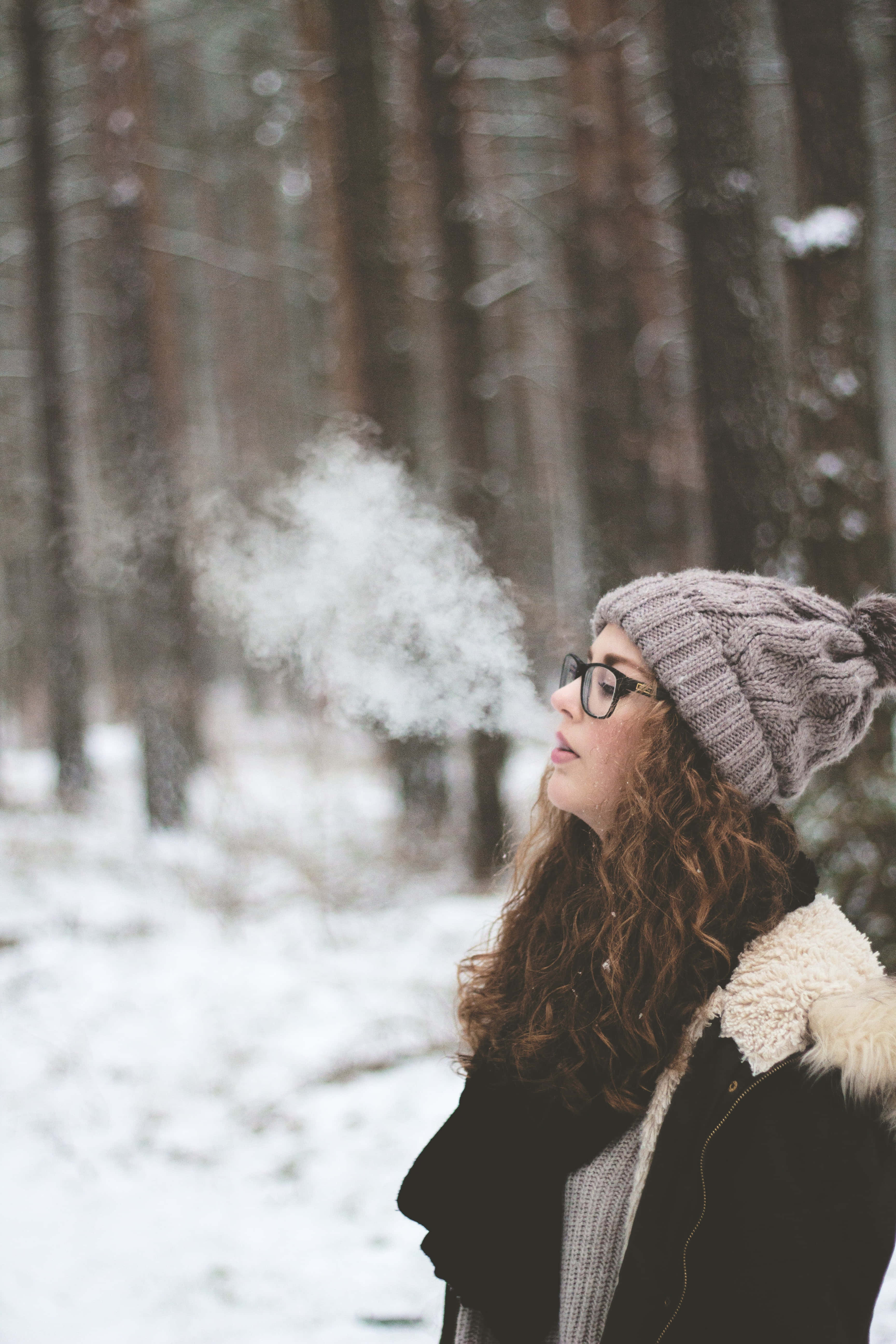 Cold 桌布 壁紙 — 一個戴著針織帽的女人向寒冷積雪的森林呼出溫暖的氣息，她的眼鏡起霧，捲髮勾勒出她的臉龐。