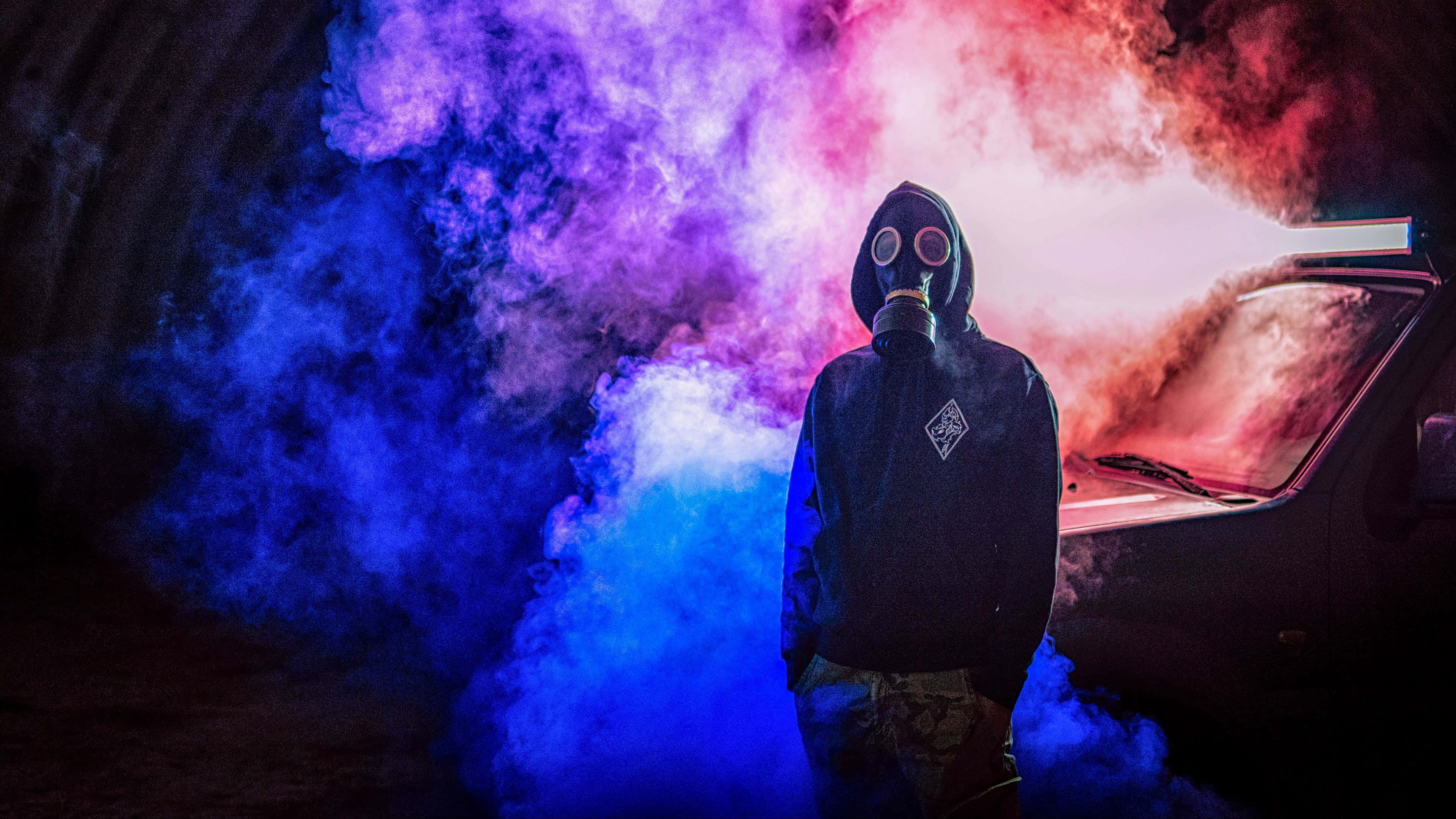 Mask 桌布 壁紙 — 一個戴著防毒面具的人站在隧道內，被鮮豔的藍色和紅色煙霧包圍，附近有一輛車。