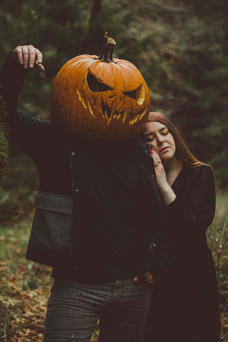 Halloween Pumpkin 桌布 壁紙 — 一個戴著雕刻南瓜頭的人在秋天的黑暗森林中擁抱另一個人。
