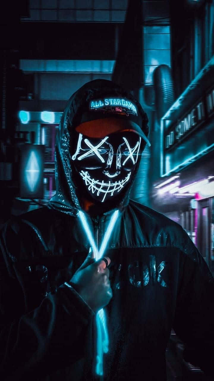 Mask 桌布 壁紙 — 一個戴著面具、身穿連帽衫的人物站在霓虹燈照亮、散發電光藍光的城市小巷中。