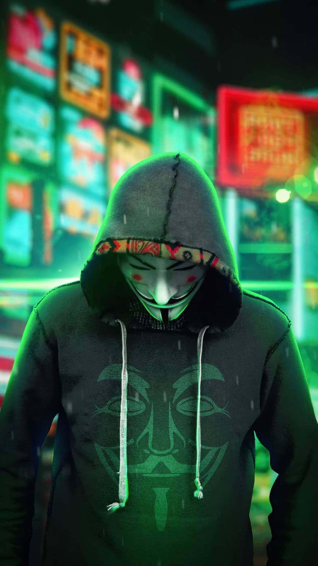 Anonymous Mask 桌布 壁紙 — 一個戴著面具、身穿連帽衫的人站在被雨水浸濕、霓虹燈閃爍的城市街道上，綠色和紅色的招牌閃閃發光。