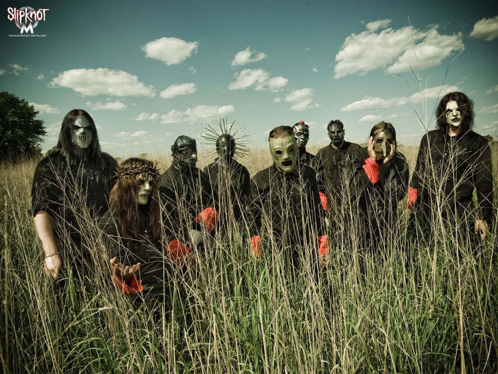 Slipknot 桌布 壁紙 — 一個戴著面具、身穿黑色服裝的樂團站在高高的草叢中，天空多雲。