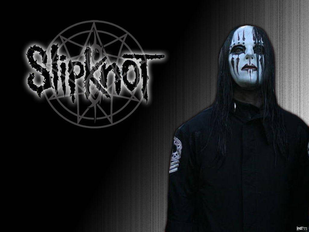 Joey Jordison 桌布 壁紙 — 一個戴著面具的Slipknot樂團成員站在深色紋理牆壁旁，旁邊是帶有發光邊緣的樂團標誌。