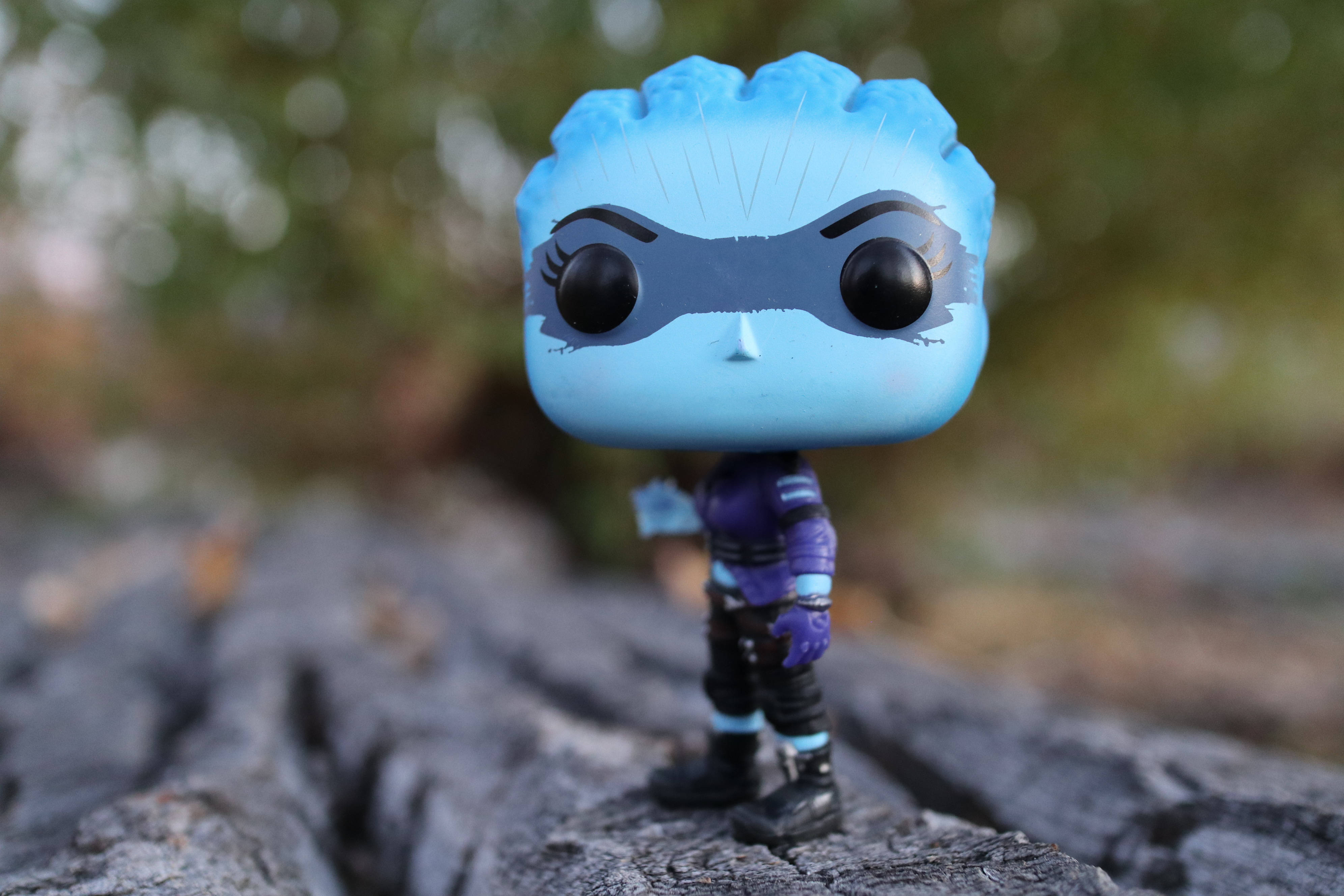 pop 桌布 壁紙 — 一個戴著面具的藍色Funko Pop公仔站在風化的木頭上，背景是模糊的自然景色。