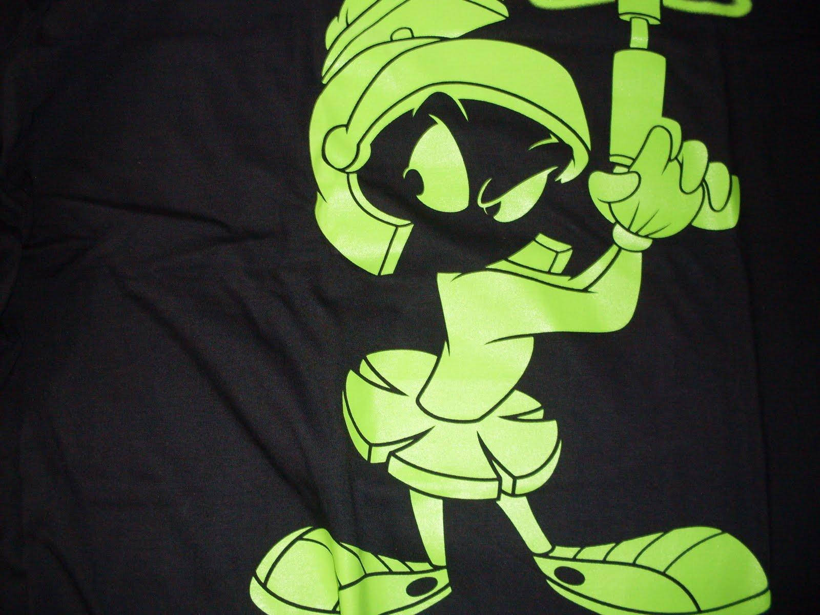 Marvin The Martian 桌布 壁紙 — 一個戴著頭盔和靴子的明亮螢光綠色卡通角色，在黑色布料背景前拿著工具。