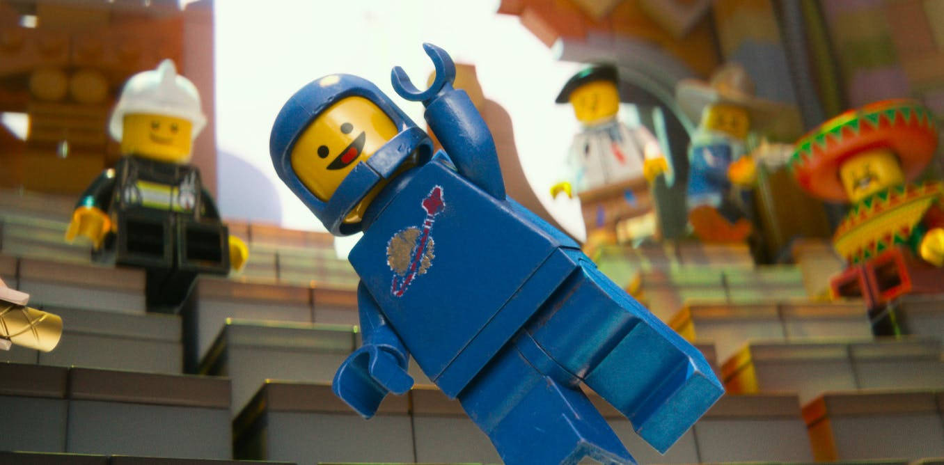 電影動圖 桌布 壁紙 — 一個戴著頭盔的藍色LEGO迷你人偶，在其他色彩繽紛的LEGO人偶組成的體育場上空，高舉雙臂，歡樂地跳躍。
