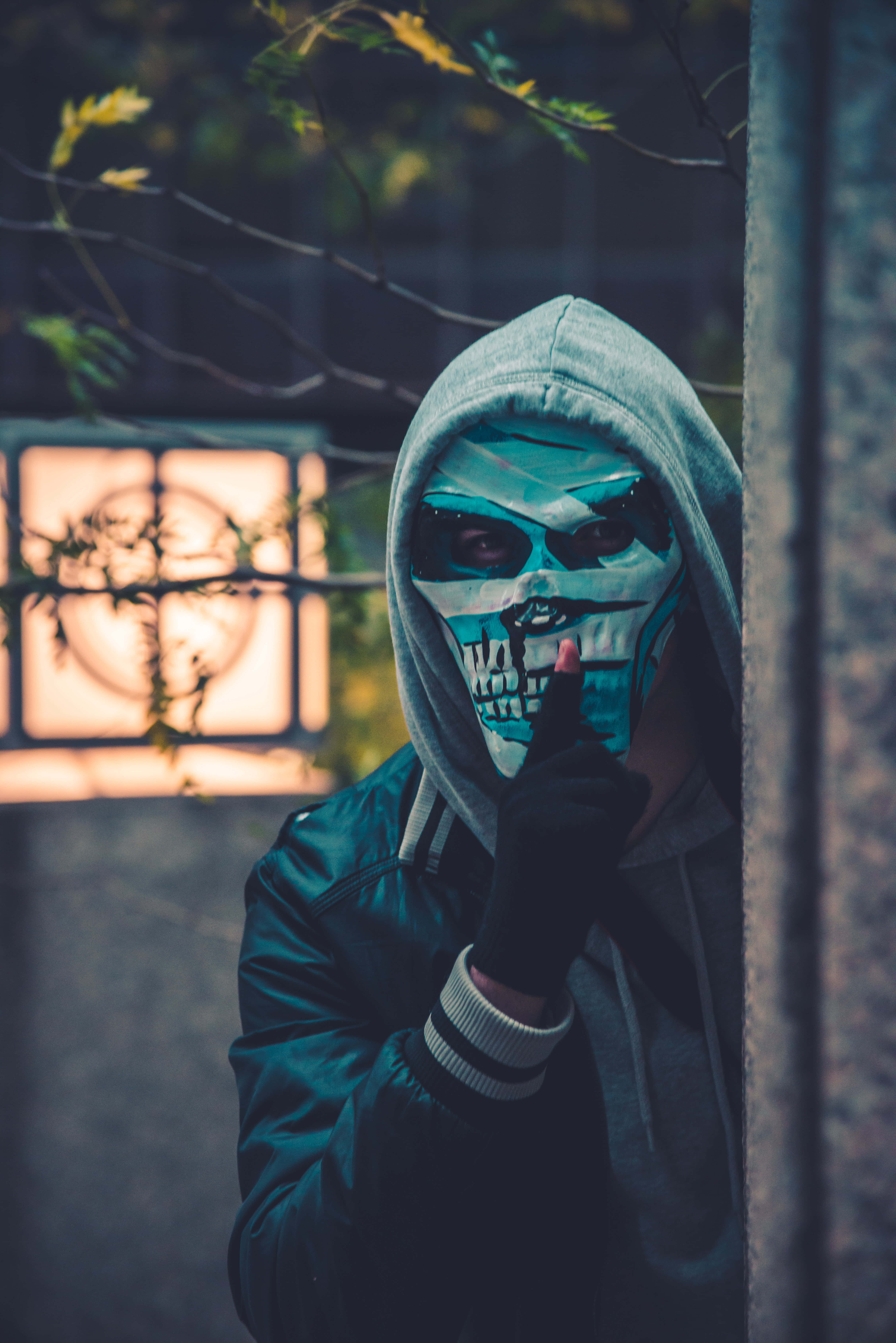 Mask 桌布 壁紙 — 一個戴著骷髏面具和連帽衫的人在黃昏時分從牆後探出頭來，手指放在嘴唇上。