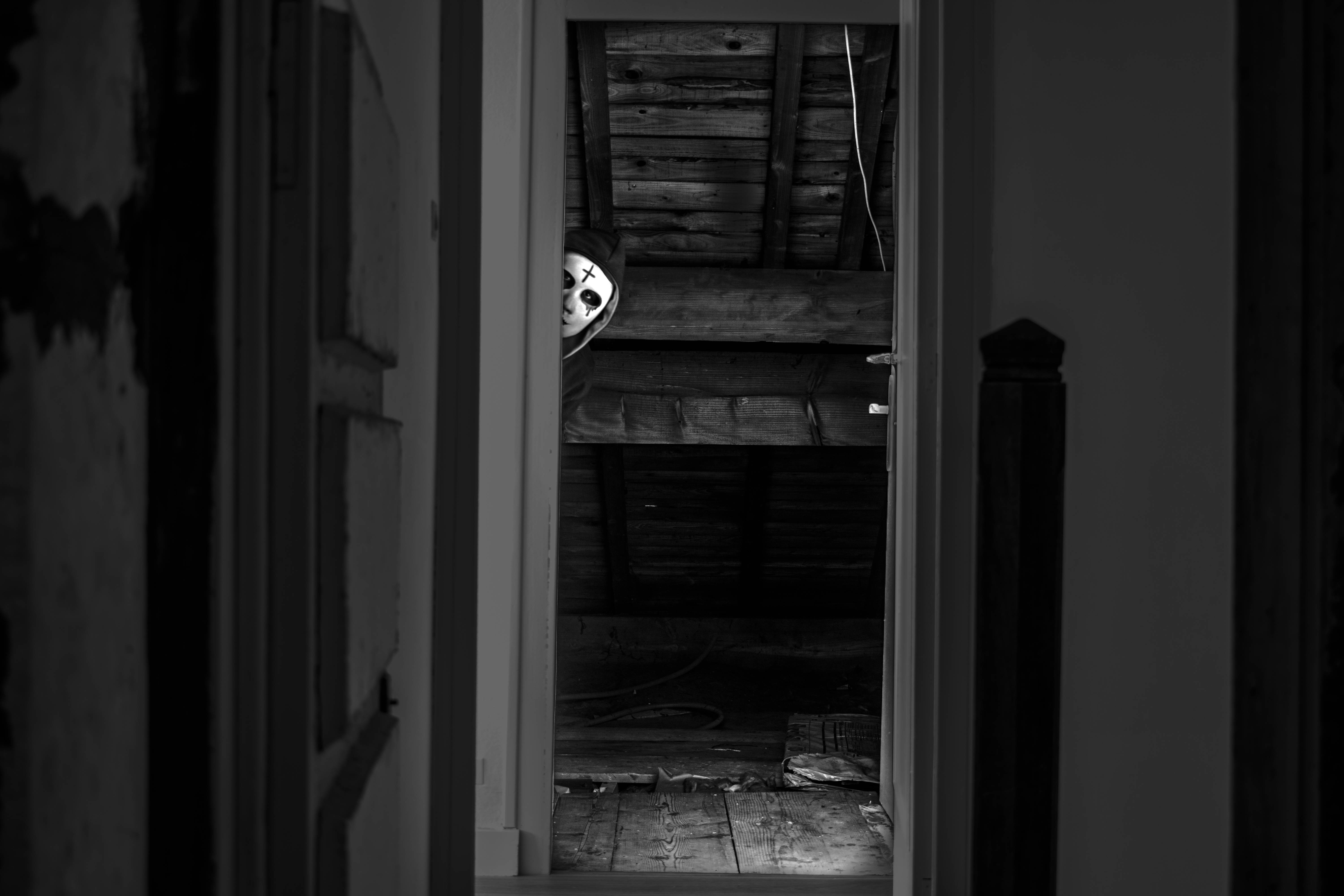 Paranormal 桌布 壁紙 — 一個戴著骷髏面具的鬼影從黑暗的閣樓門口窺視，呈現單色恐怖場景。