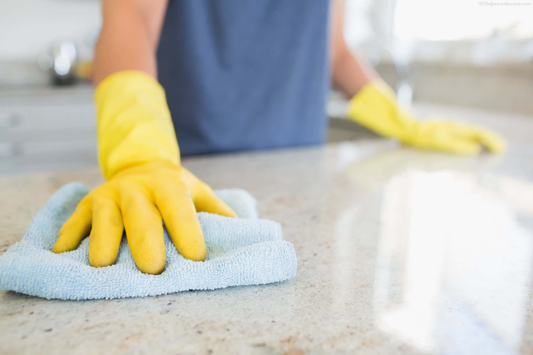 Cleaning 桌布 壁紙 — 一個戴著黃色手套的人在明亮的廚房裡用淺藍色布擦拭一個有斑點的檯面。