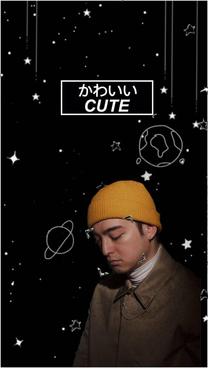 joji 桌布 壁紙 — 一個戴著黃色毛帽的年輕男子向下凝視，背景是星空的黑色背景，上面有塗鴉的行星和「cute」這個詞。