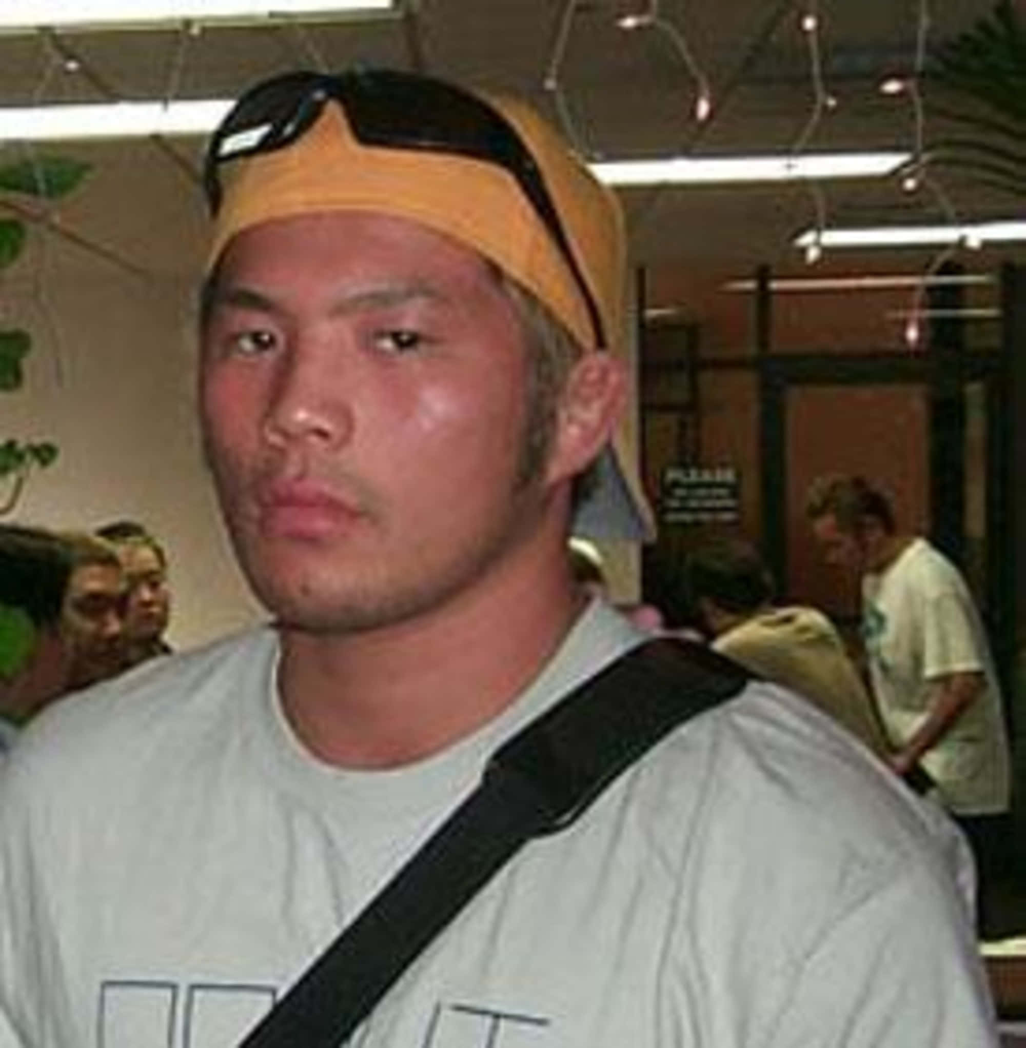 MMA 桌布 壁紙 — 一個戴著黃色鴨舌帽和太陽眼鏡擱在頭上的男人，在光線明亮的室內環境中直視鏡頭。