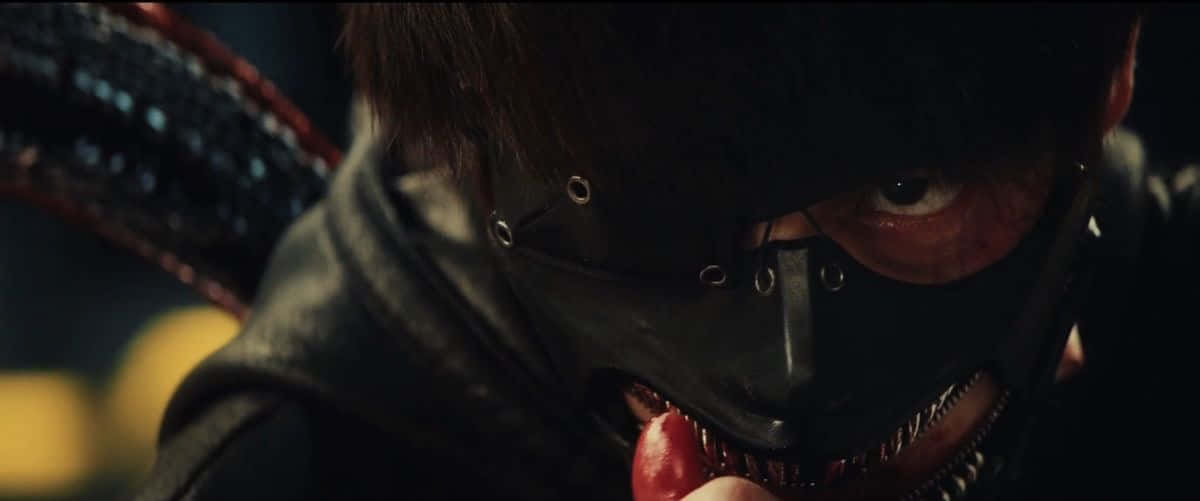 Tokyo Ghoul Movie 桌布 壁紙 — 一個戴著黑色皮革面具和尖牙的蒙面動漫角色在黑暗場景中咬著一個紅色物體。