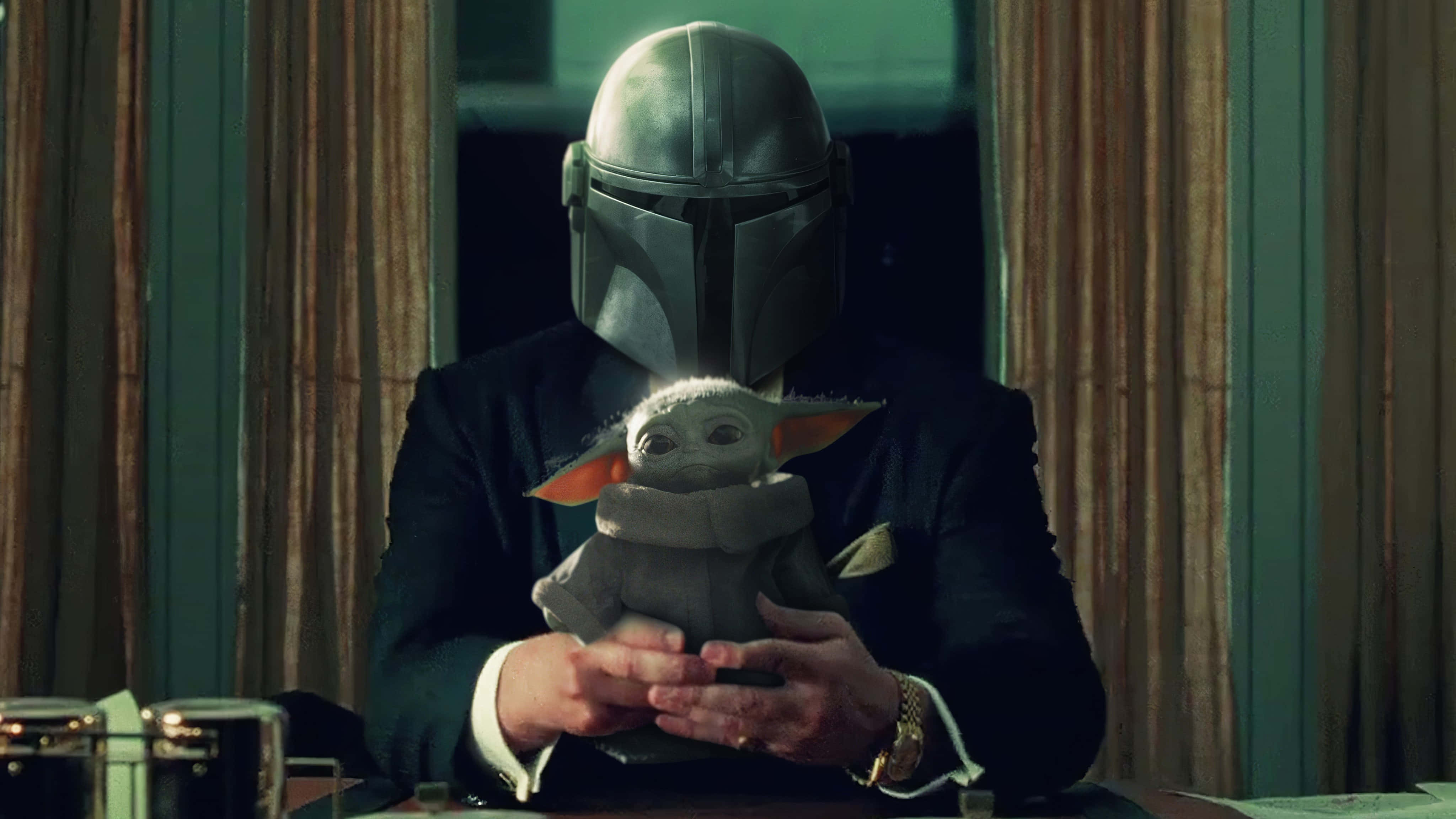 Mandalorian Yoda 桌布 壁紙 — 一個戴面具、身穿西裝的人物，在燈光昏暗的桌子旁，輕輕搖晃著一個有大耳朵和連帽斗篷的小毛茸茸生物。