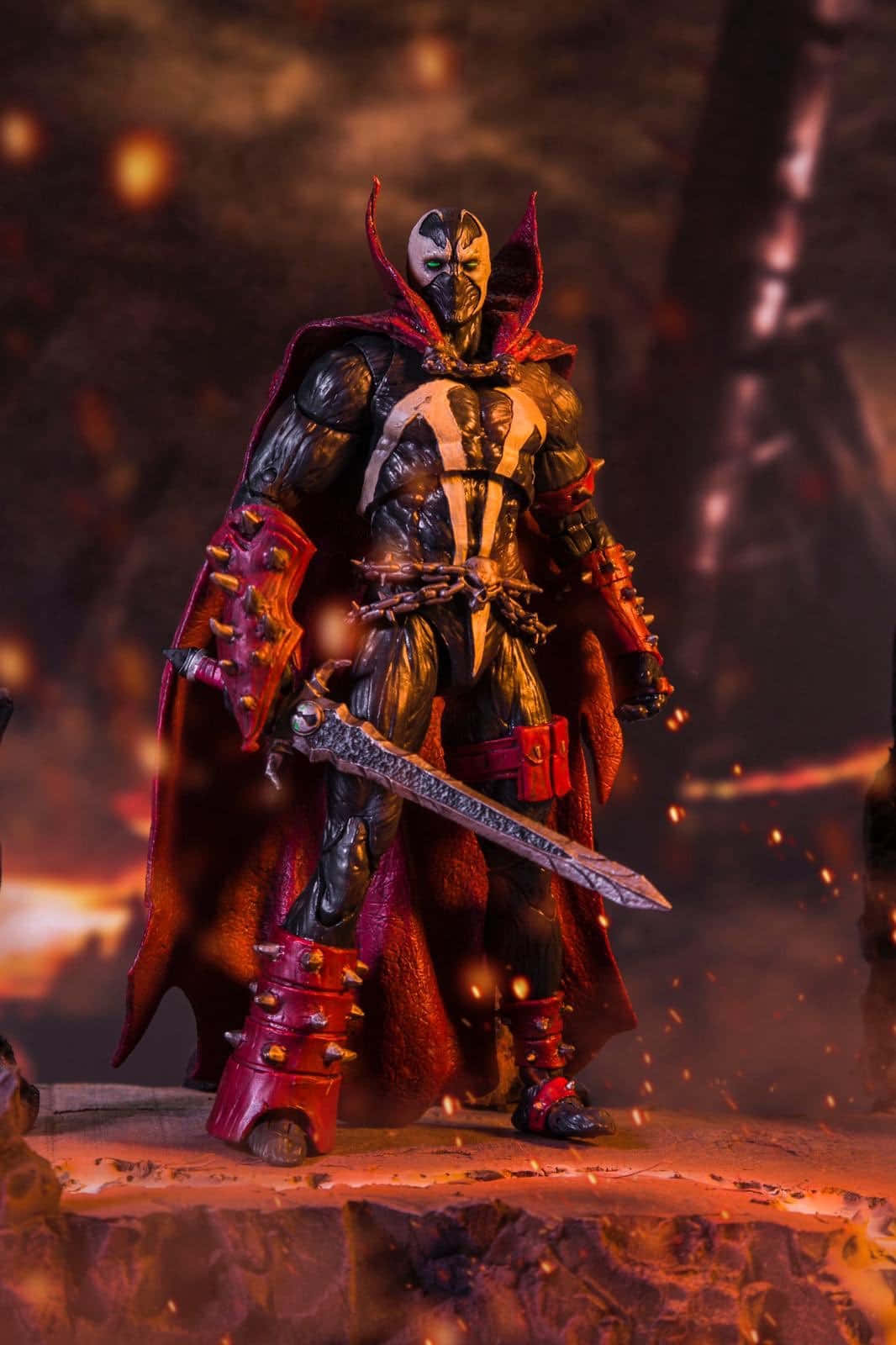 Mortal Kombat 11 Spawn 桌布 壁紙 — 一個戴面具的戰士，身穿黑色和紅色盔甲，手持劍，在熾熱的火花和發光的餘燼中擺出威脅姿勢的動作人偶。
