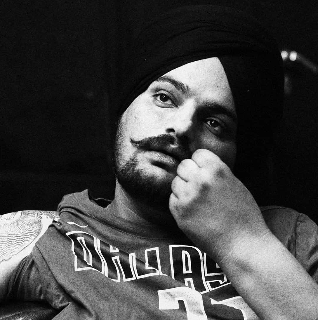一個戴頭巾和連帽衫的男人，在黑白照片中拳頭托著下巴。 — Sidhu Moose Wala 壁紙