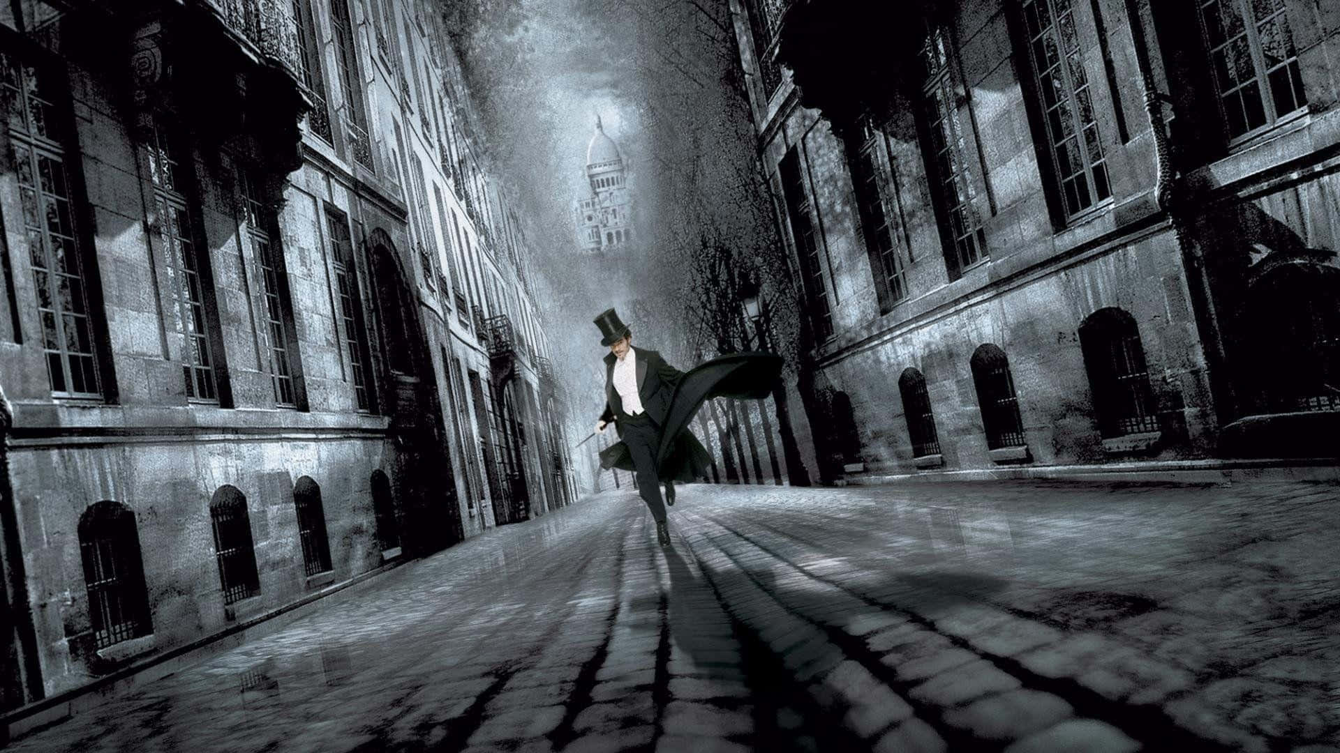 Arsène Lupin 桌布 壁紙 — 一個戴高帽、穿大衣的孤獨身影，在陰沉天空下，沿著兩旁高聳哥德式建築的霧氣籠罩鵝卵石街道大步前行。