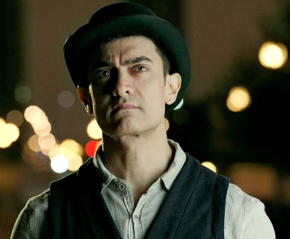 Aamir Khan 桌布 壁紙 — 一個戴黑色圓頂禮帽的男人，在模糊的夜景和發光散景燈光中凝視著。