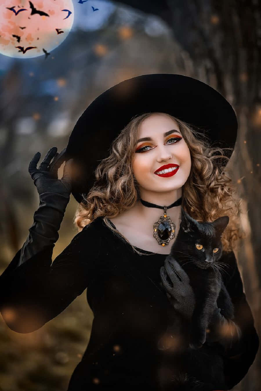 Witch Costumes 桌布 壁紙 — 一個戴黑色巫師帽和手套的女人，在發光的粉紅月亮下抱著一隻黑貓，蝙蝠在飛翔。