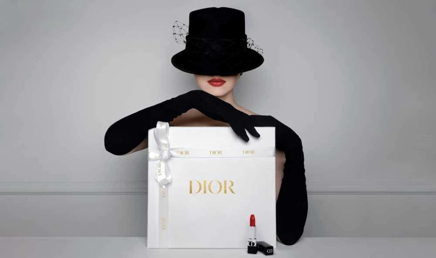 戴黑色帽子和手套的人體模型拿著Dior禮品盒和紅色唇膏。 — Dior 動態 壁紙