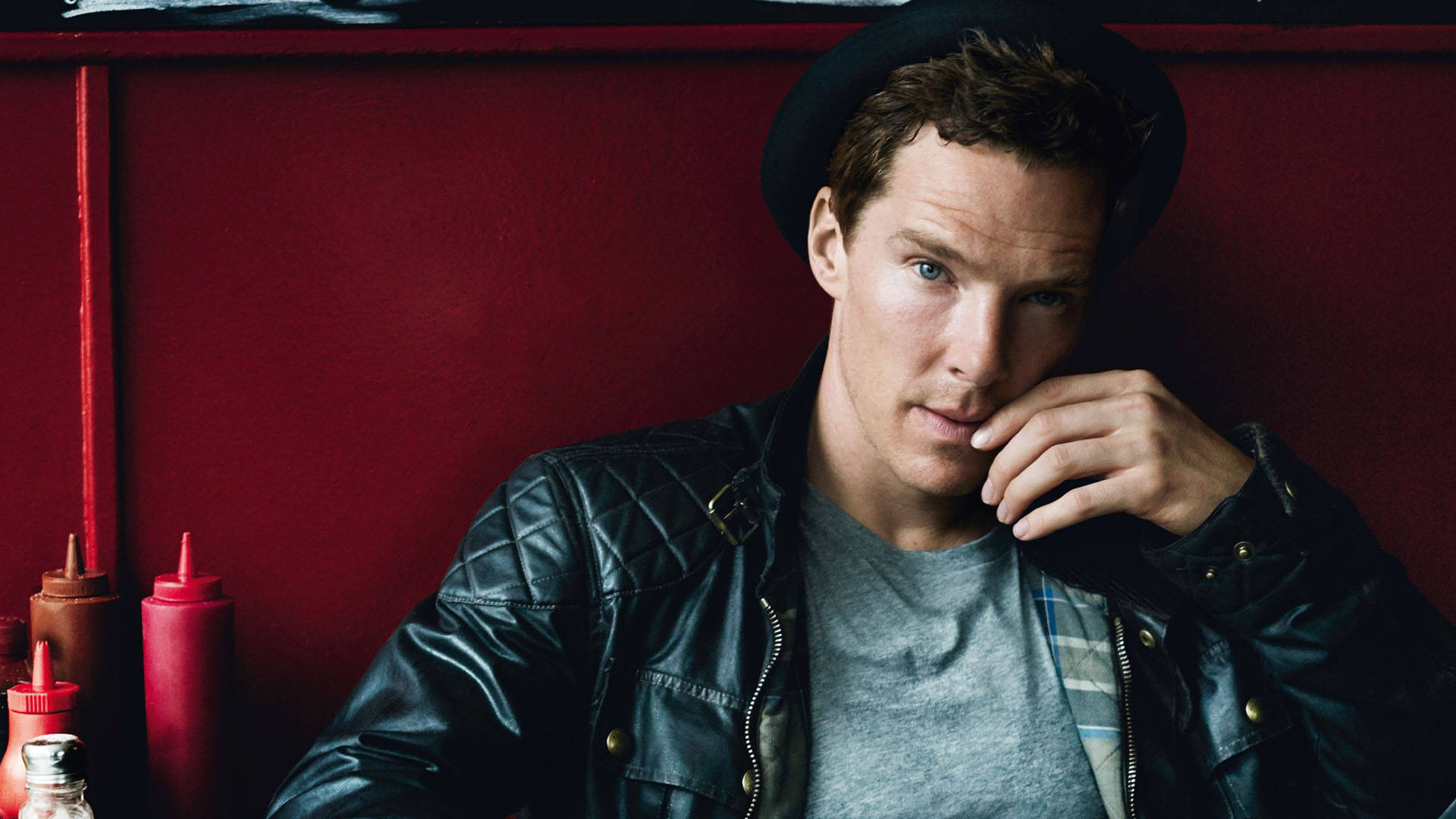 benedict 桌布 壁紙 — 一個戴黑色帽子和皮夾克的男人，將下巴擱在手上，靠著一個鮮紅色、放有調味瓶的餐廳牆壁。