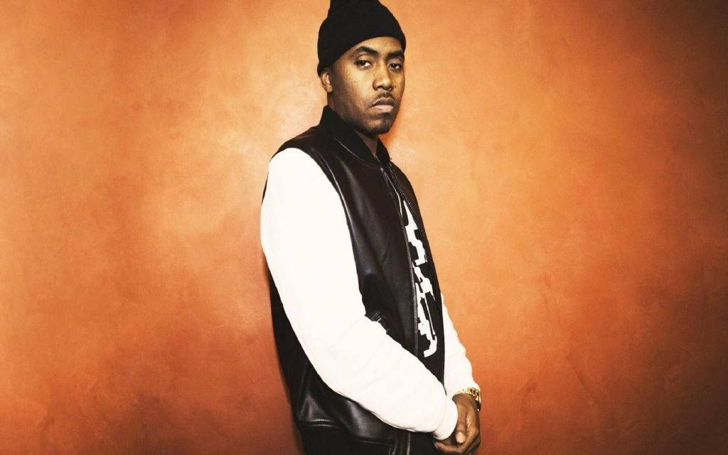 90s Rapper 桌布 壁紙 — 一個戴黑色毛帽、穿皮背心的男人自信地站在溫暖的橙色紋理牆前。