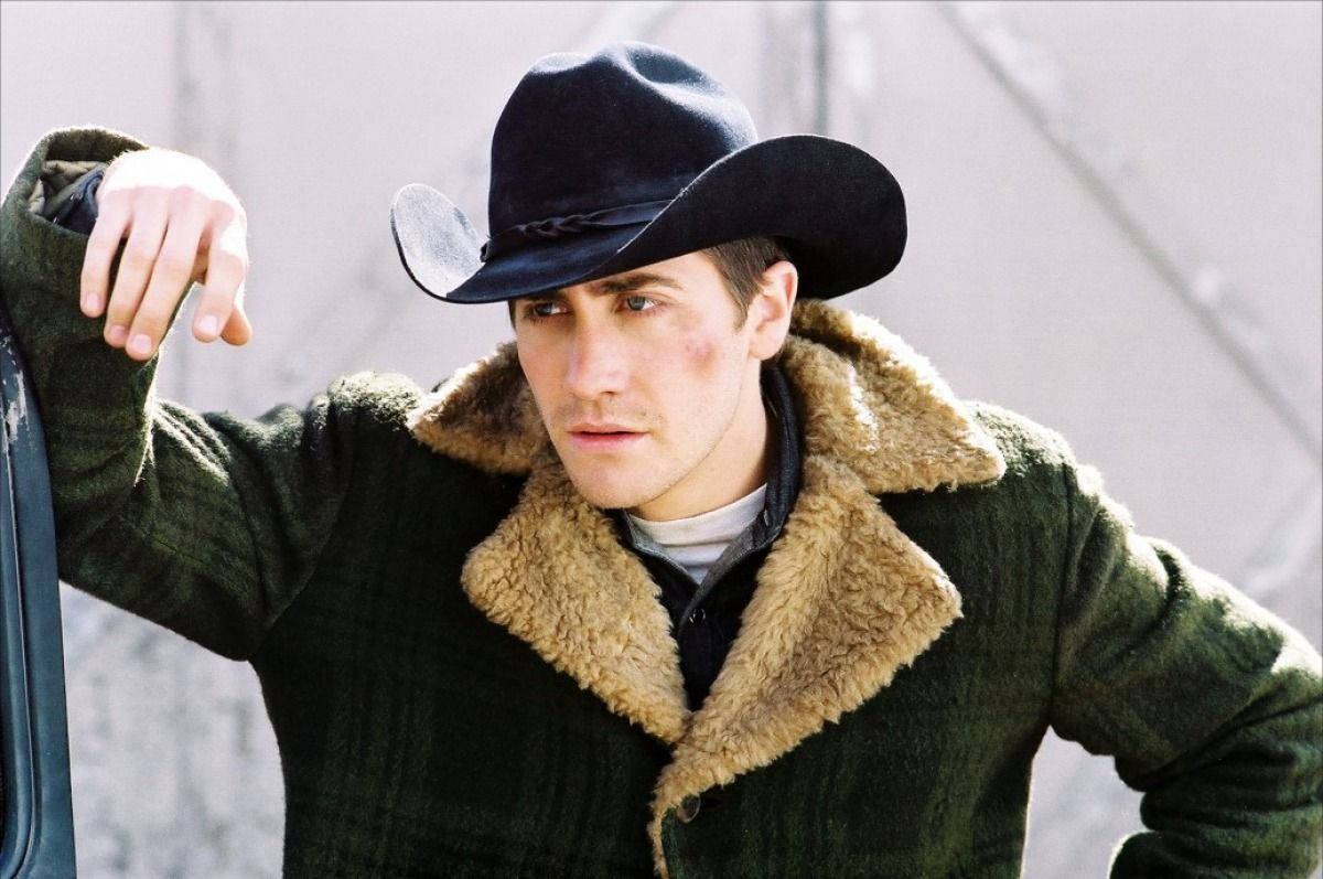 brokeback mountain 桌布 壁紙 — 一個戴黑色牛仔帽、穿綠色羊羔絨外套的男人，表情嚴肅地靠在一輛車上。