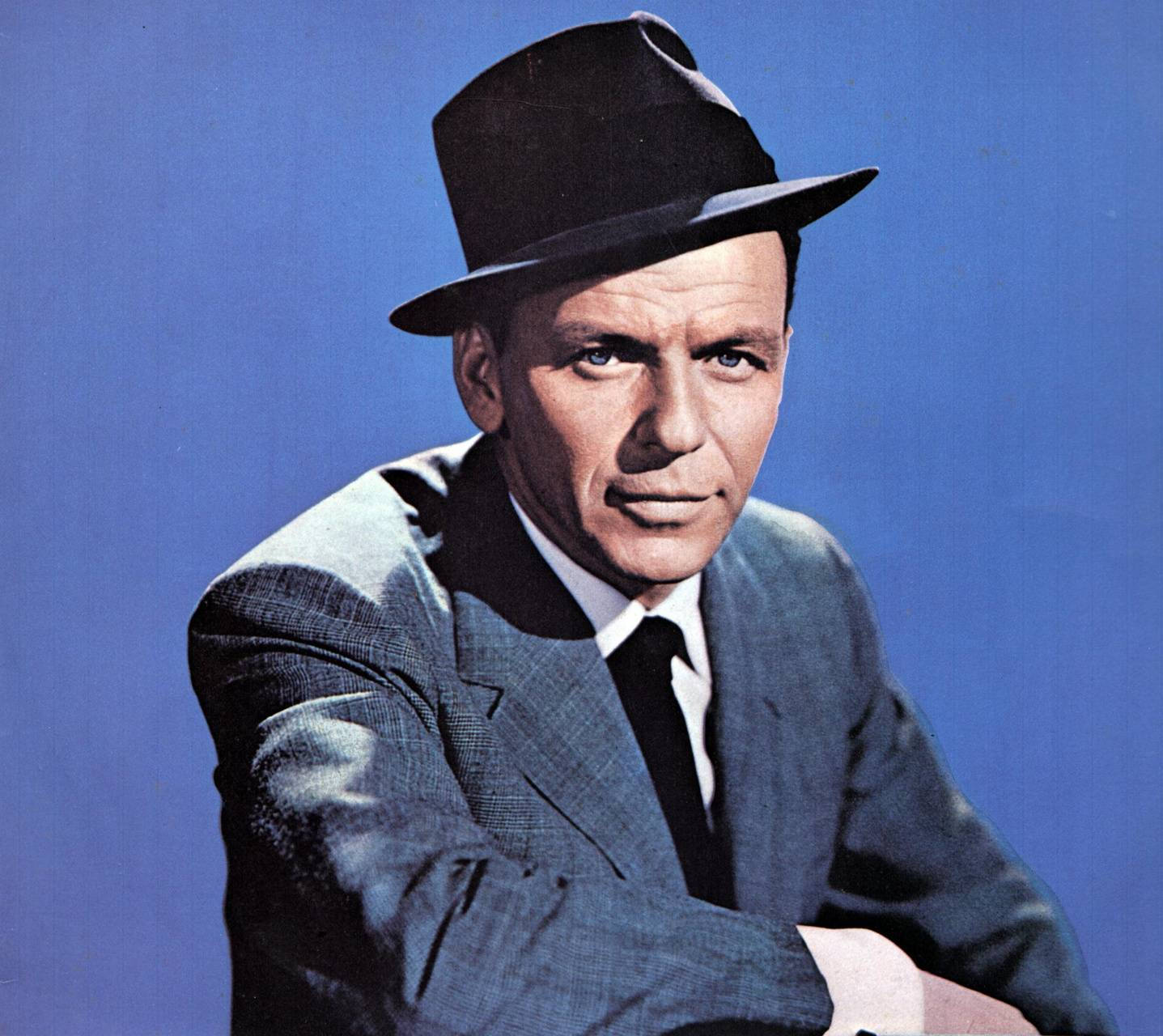 Sinatra 桌布 壁紙 — 一個戴黑色紳士帽、穿灰色西裝的男人在純藍色攝影棚背景前交叉雙臂擺姿勢。
