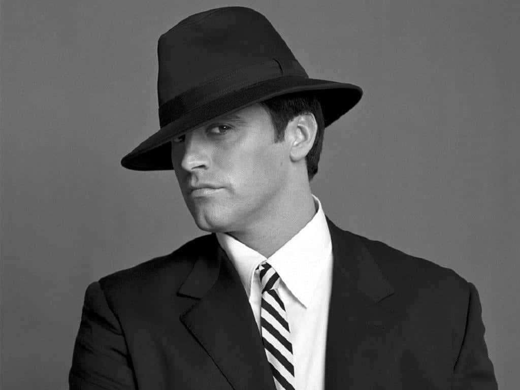 Matt Leblanc 桌布 壁紙 — 一個戴黑色紳士帽、穿西裝的男人，在純灰色背景前側視，表情嚴肅。