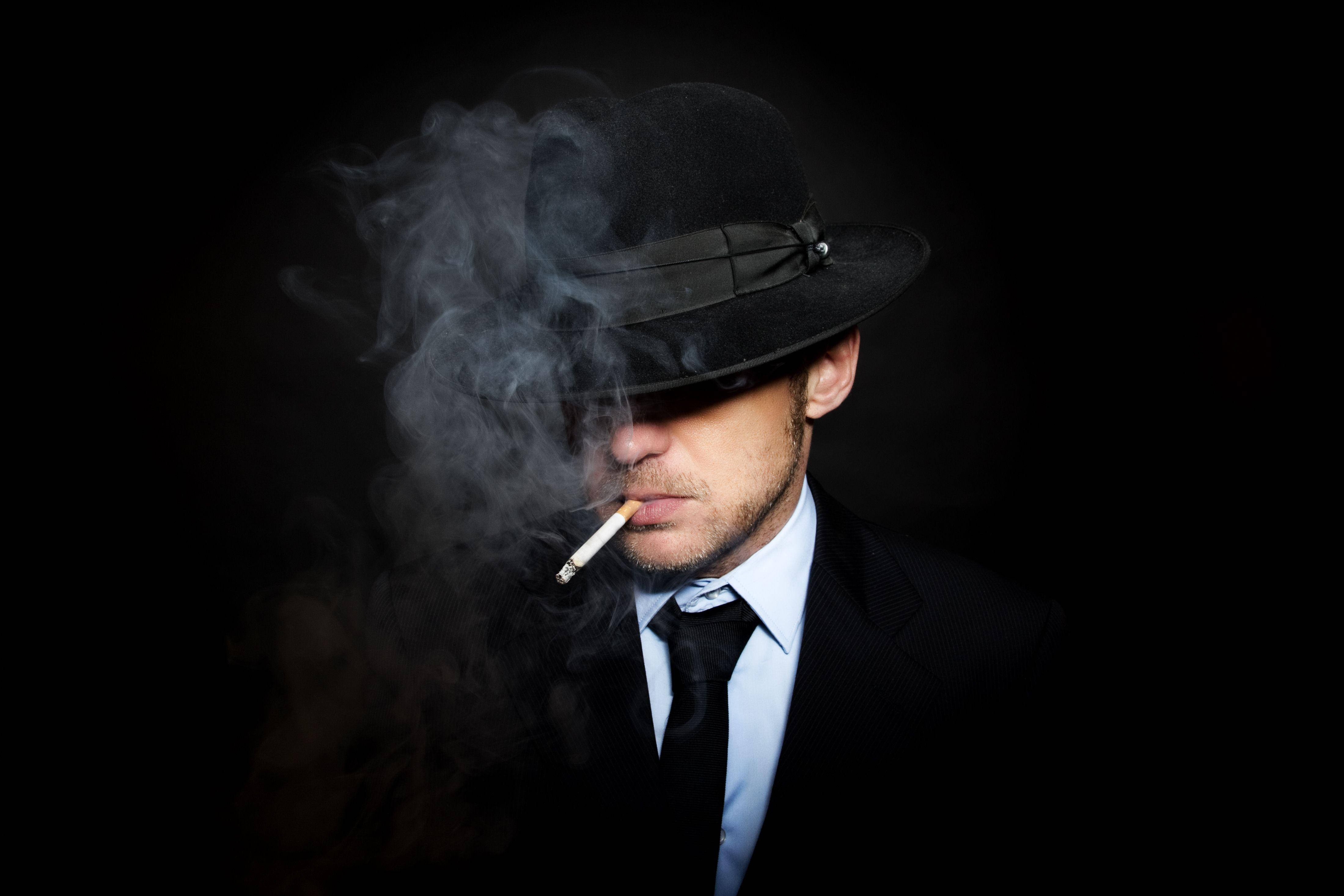 Smoking 桌布 壁紙 — 一個戴黑色軟呢帽、穿西裝的男人在黑暗背景中抽煙，煙霧繚繞。