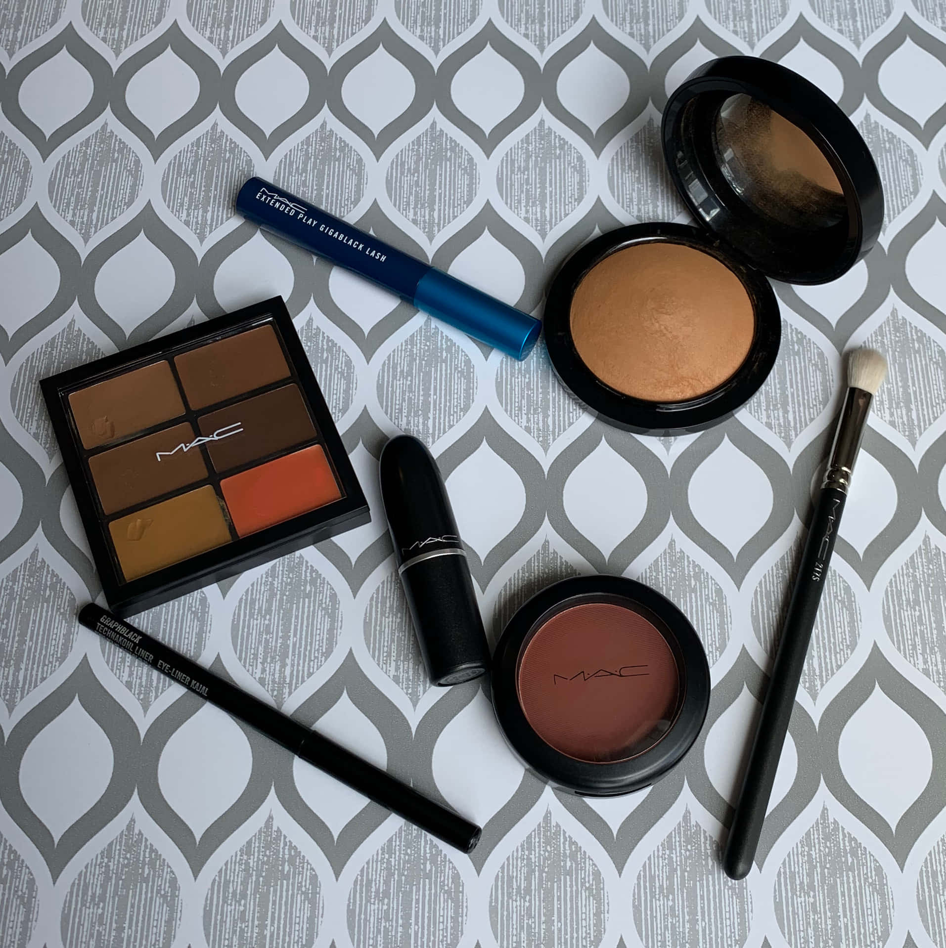 Mac Cosmetics 桌布 壁紙 — 一個扁平佈局的MAC化妝品，包括眼影、腮紅和唇膏，排列在灰色和白色圖案表面上。