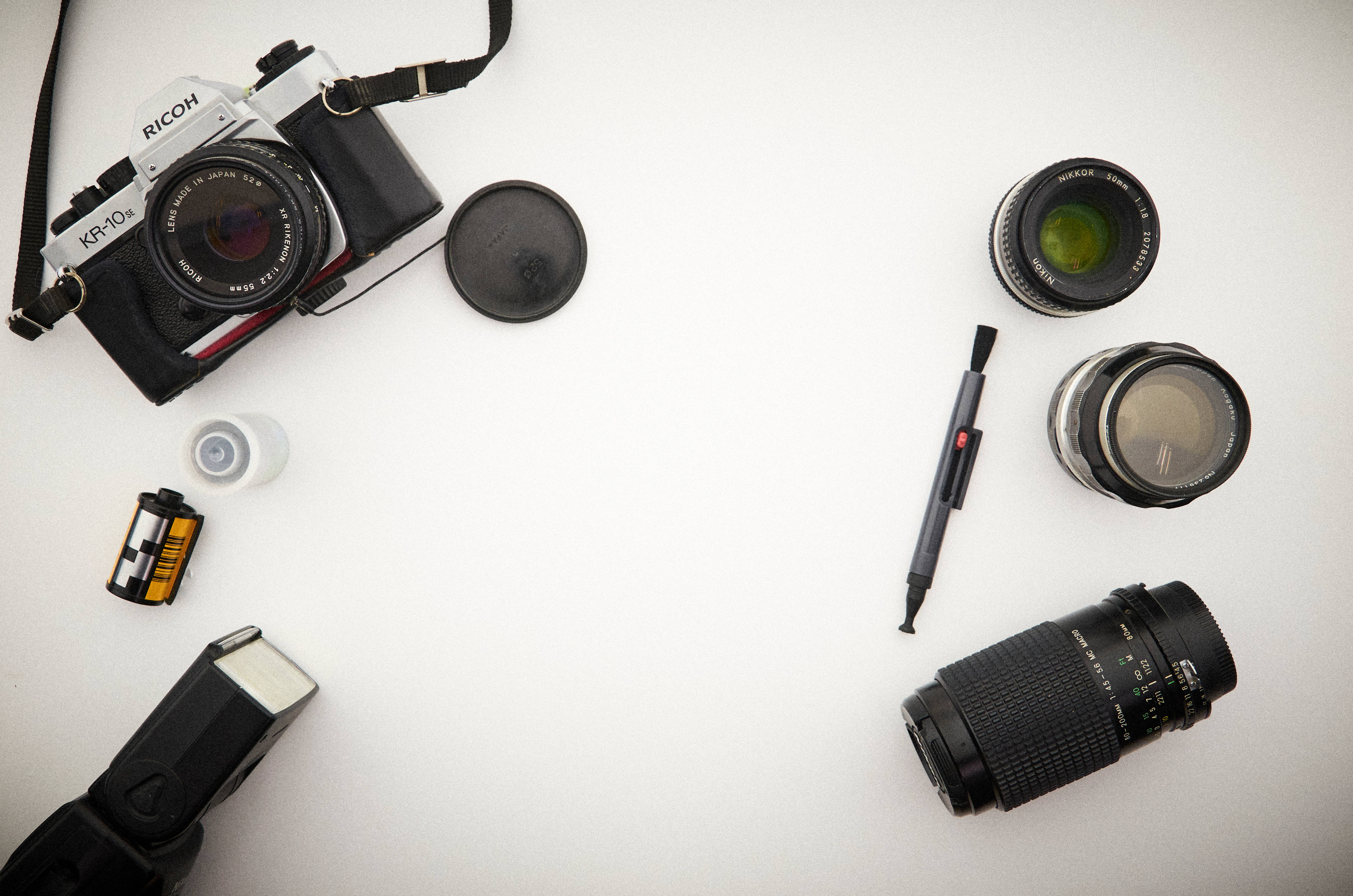 相機 桌布 壁紙 — 一個扁平擺放的復古相機裝備，包括 Ricoh KR-404、鏡頭、底片和筆，在潔白的表面上。