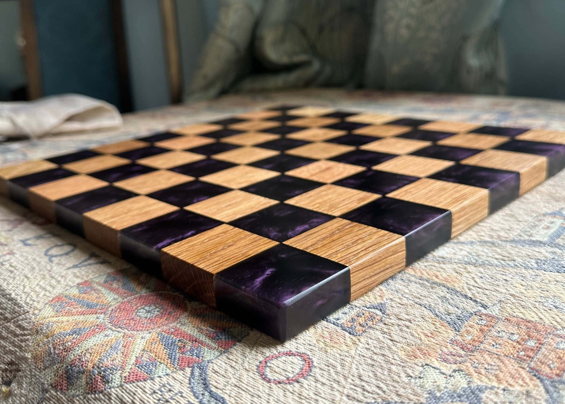 Chessboard 桌布 壁紙 — 一個手工製作的木製西洋棋棋盤，帶有紫色樹脂方格，放置在帶有圖案的紡織品表面上。