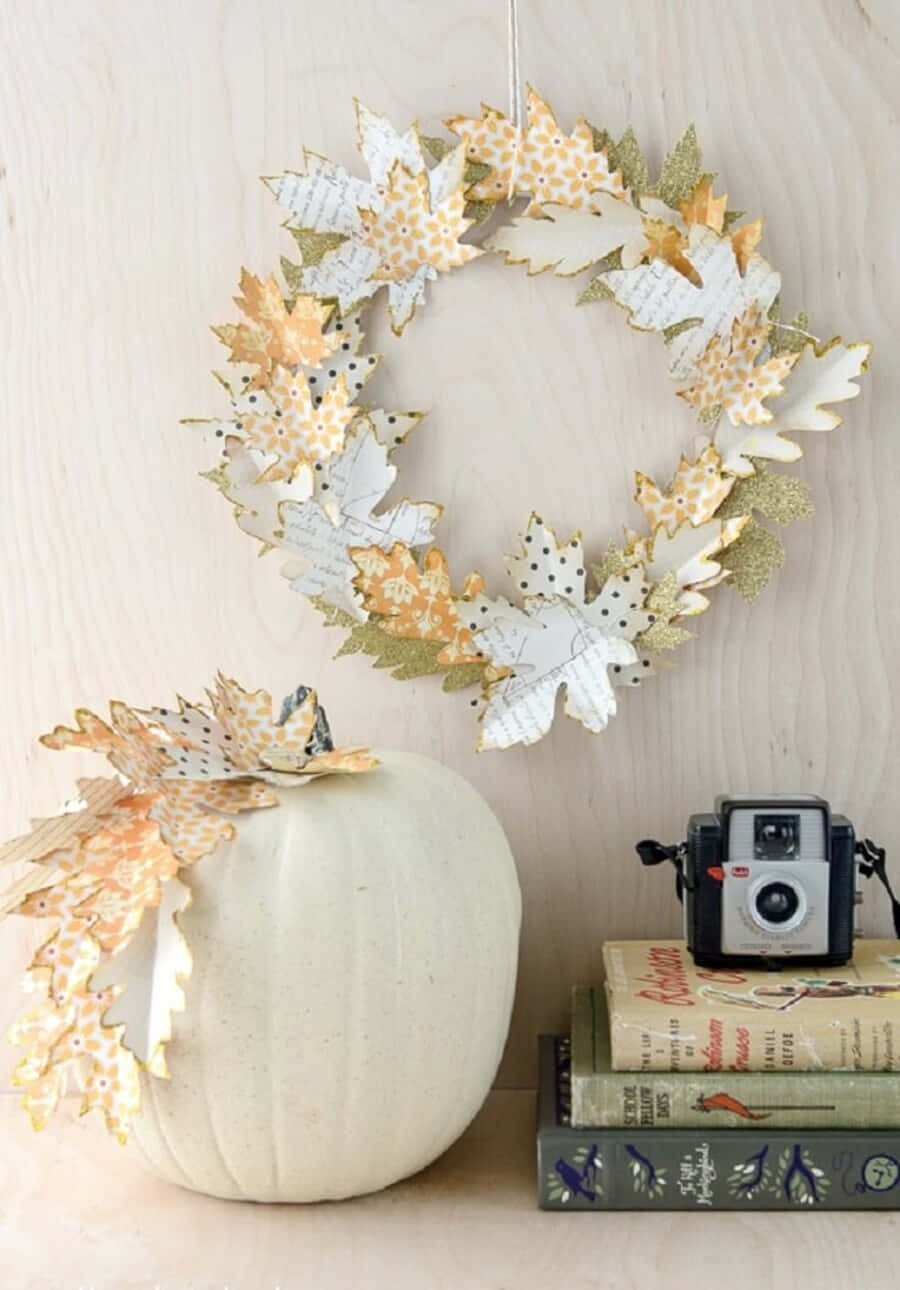 Fall Crafts 桌布 壁紙 — 一個手工製作的秋季花環和南瓜，飾有圖案紙葉，掛在復古書籍和復古相機旁邊的淺色木質表面上。