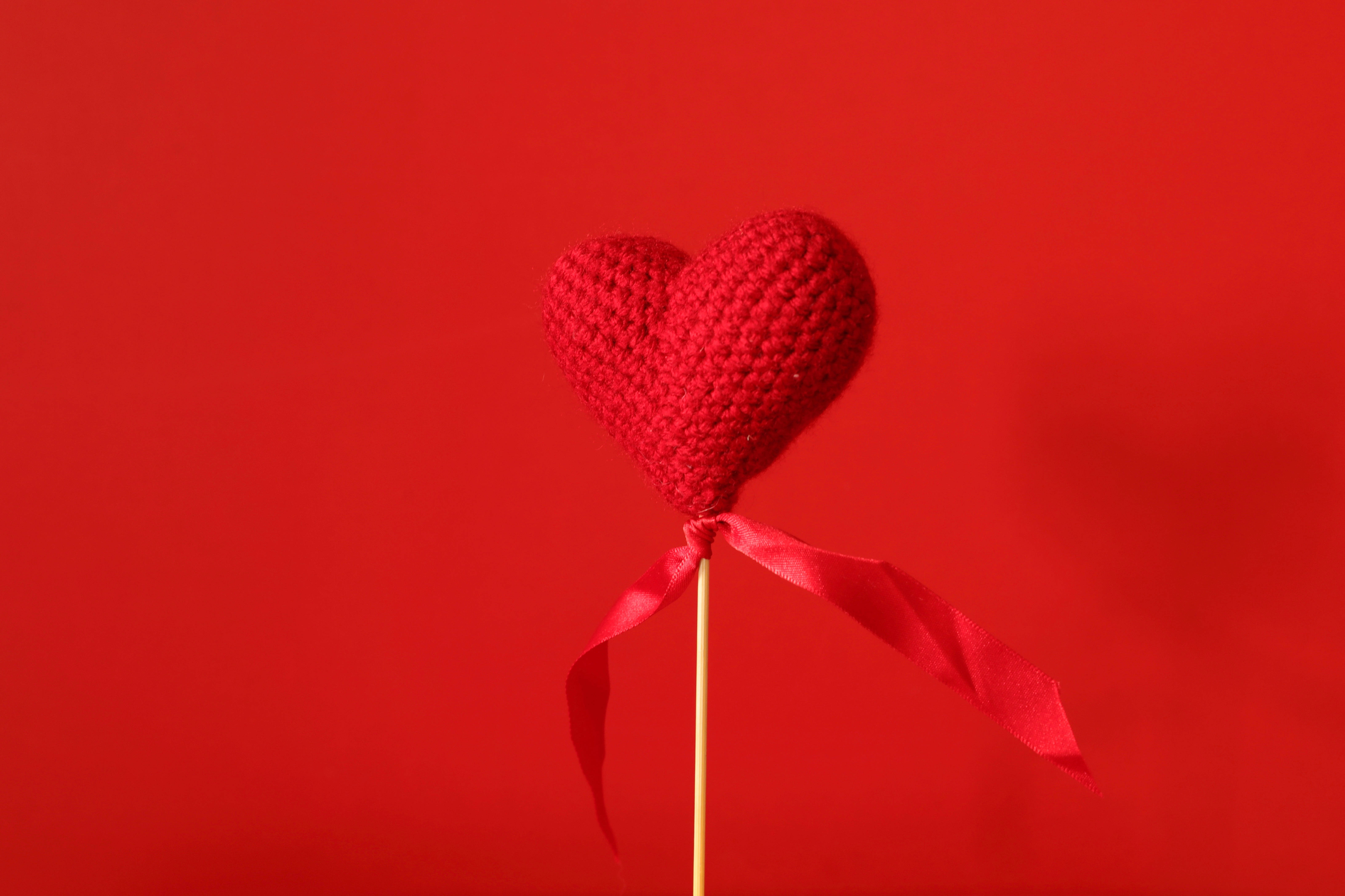 Aesthetic Heart 桌布 壁紙 — 一個手工製作的紅色鉤針編織心形，插在棒上並繫有絲帶，背景為純紅色。