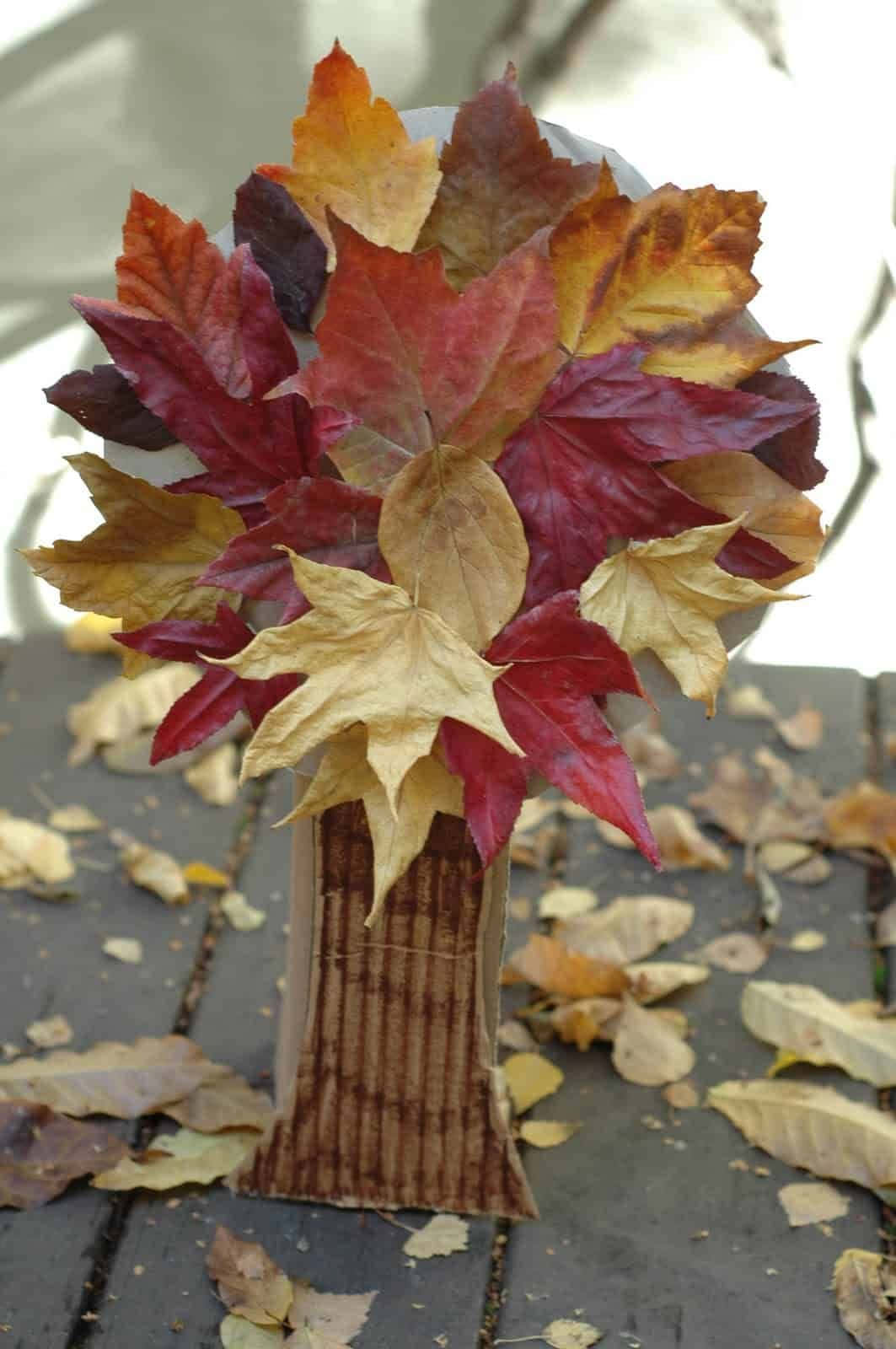 Fall Crafts 桌布 壁紙 — 一個手工製作的紙樹幹在石頭庭院上托著一束鮮豔的紅色、橙色和黃色秋葉。
