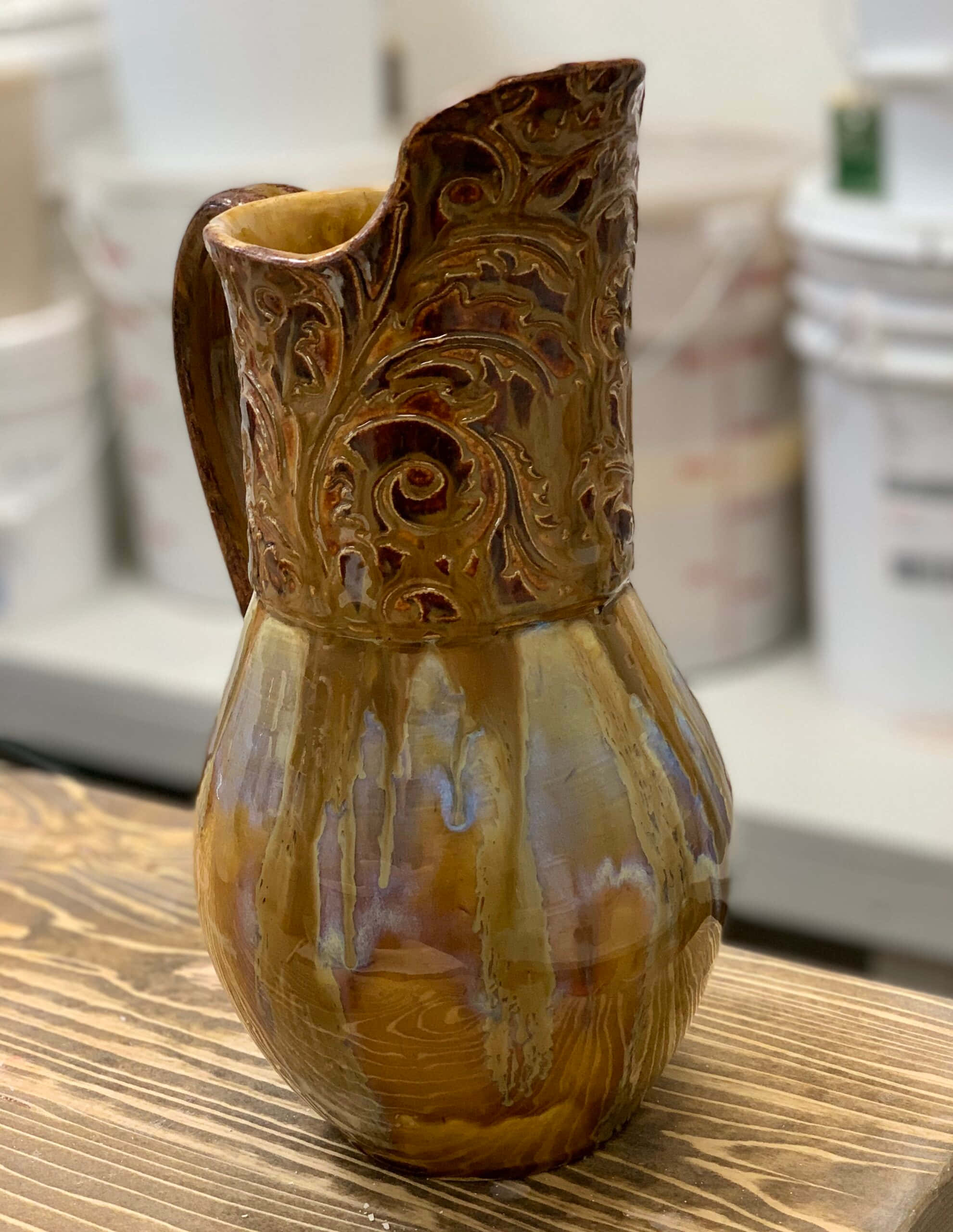 Ceramic 桌布 壁紙 — 一個手工製作的陶瓷壺，帶有複雜的棕色漩渦和光澤釉面，放在工作室的木桌上。