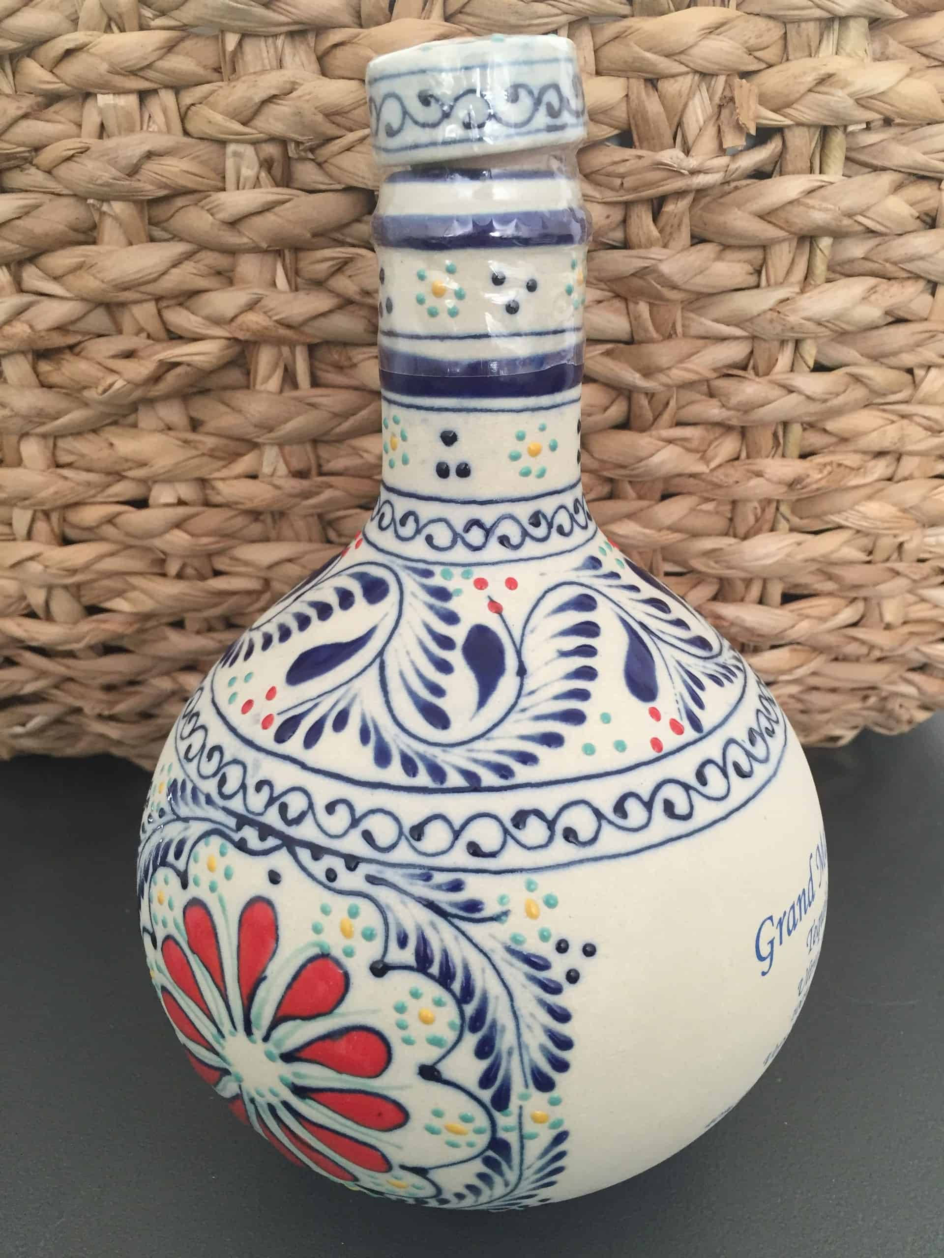 alcohol 桌布 壁紙 — 一個手繪陶瓷瓶，帶有藍色、紅色和綠色的花卉圖案，放置在深色表面上，背景是編織的柳條。