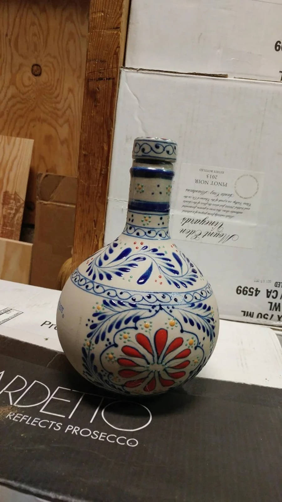 alcohol 桌布 壁紙 — 一個手繪陶瓷瓶，帶有藍色花卉圖案和一朵紅花，放在一個木製背景的酒箱上。
