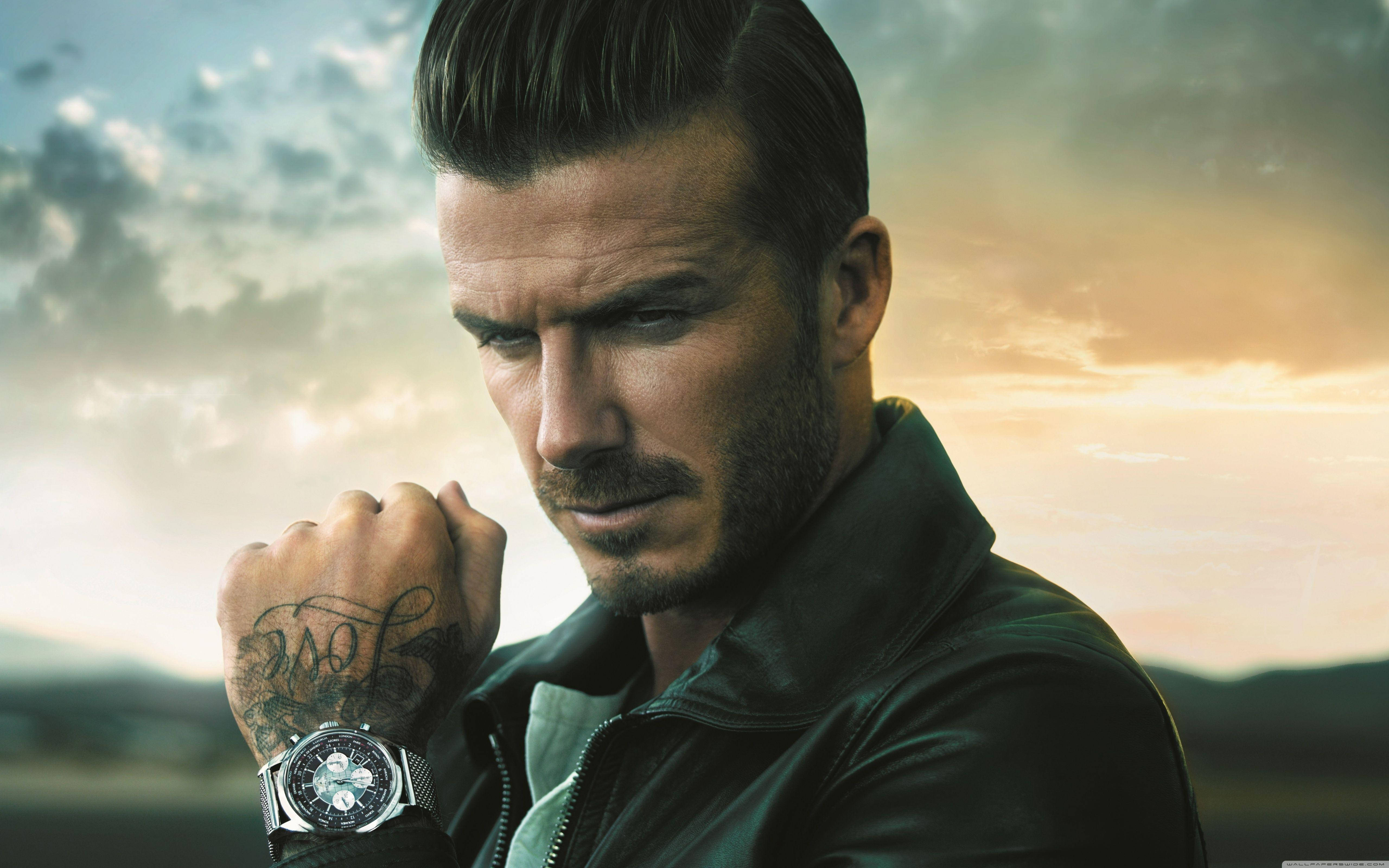 David Beckham 桌布 壁紙 — 一個手腕有刺青、身穿皮夾克的男人，在戲劇性的日落天空下凝視。