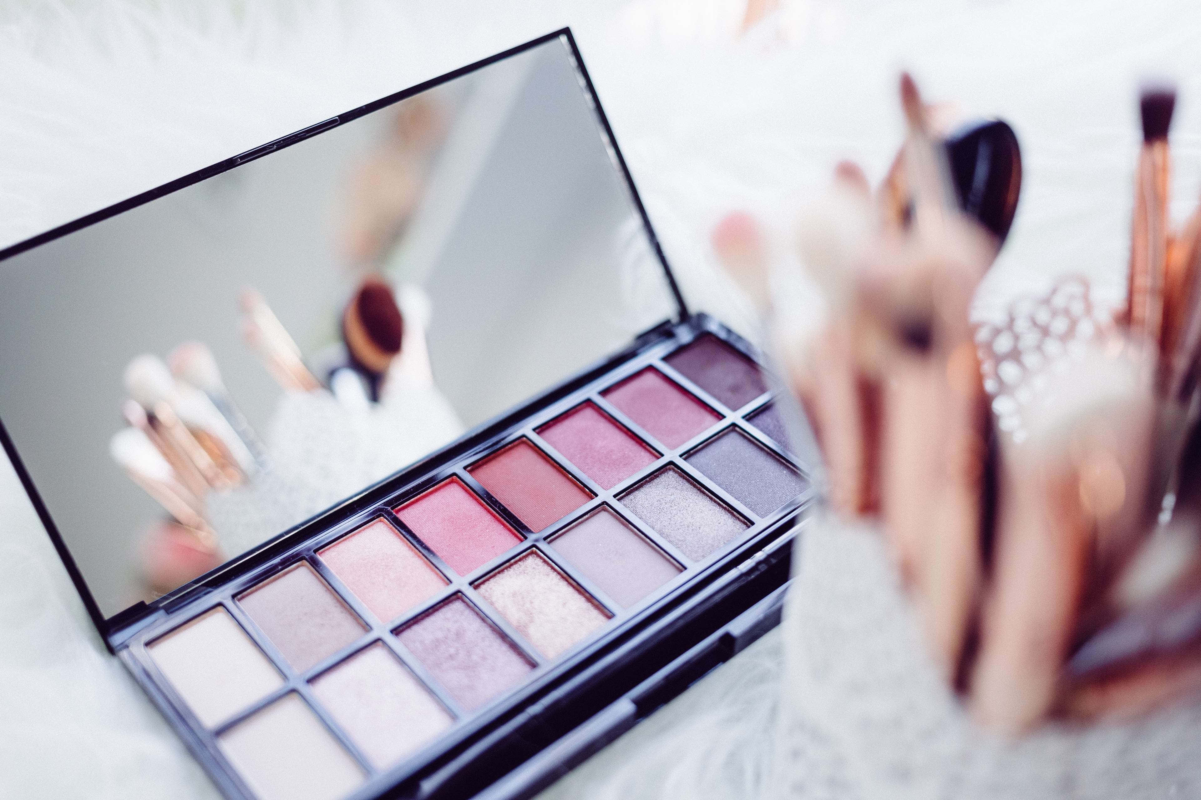 Cosmetics 桌布 壁紙 — 一個打開的眼影盤特寫，玫瑰色和紫紅色調在鏡中反射，周圍是模糊的化妝刷。