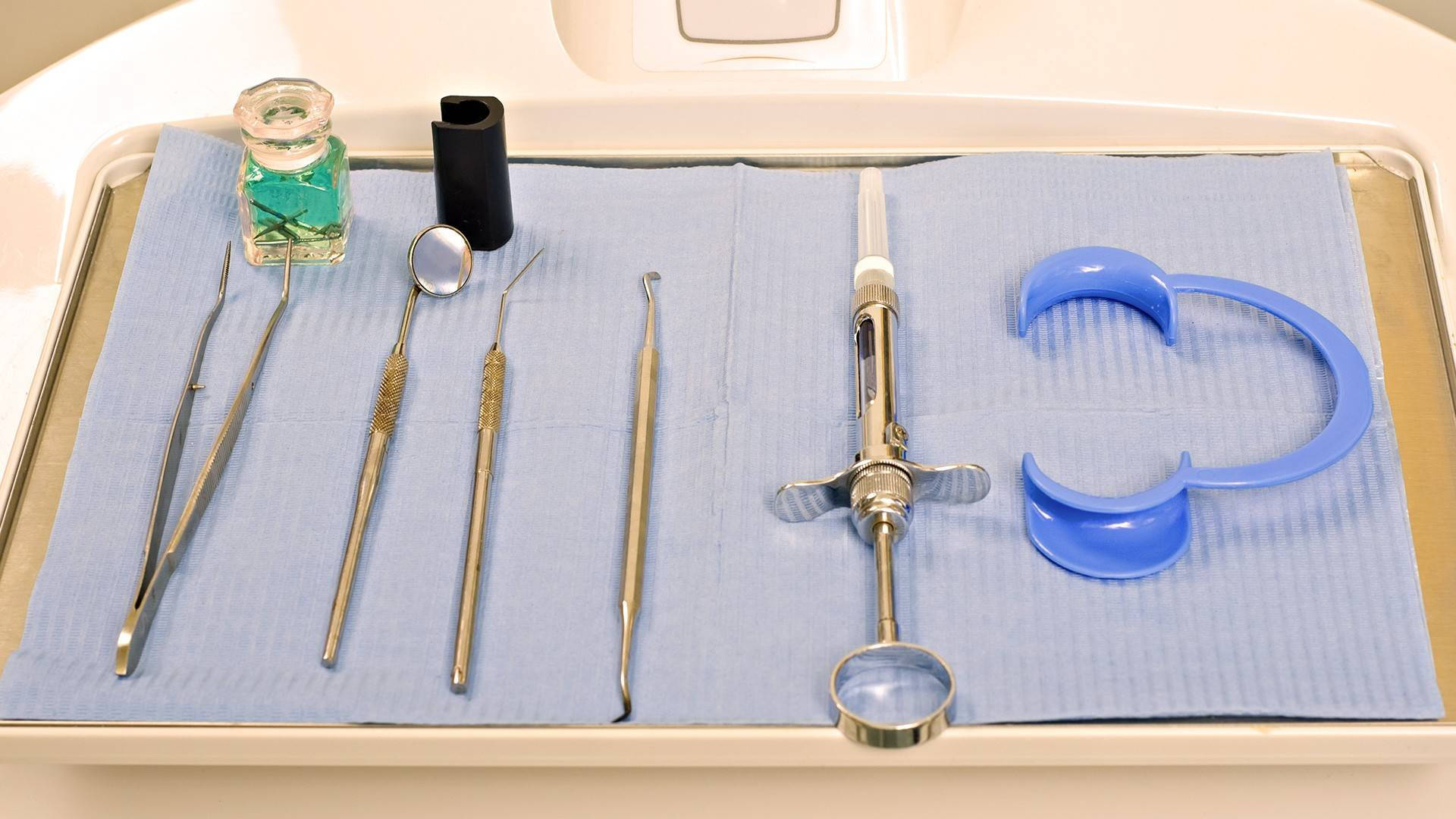 Dentistry 桌布 壁紙 — 一個托盤上放有牙科工具，包括鏡子、鑷子和注射器，排列在臨床環境中的藍色布上。