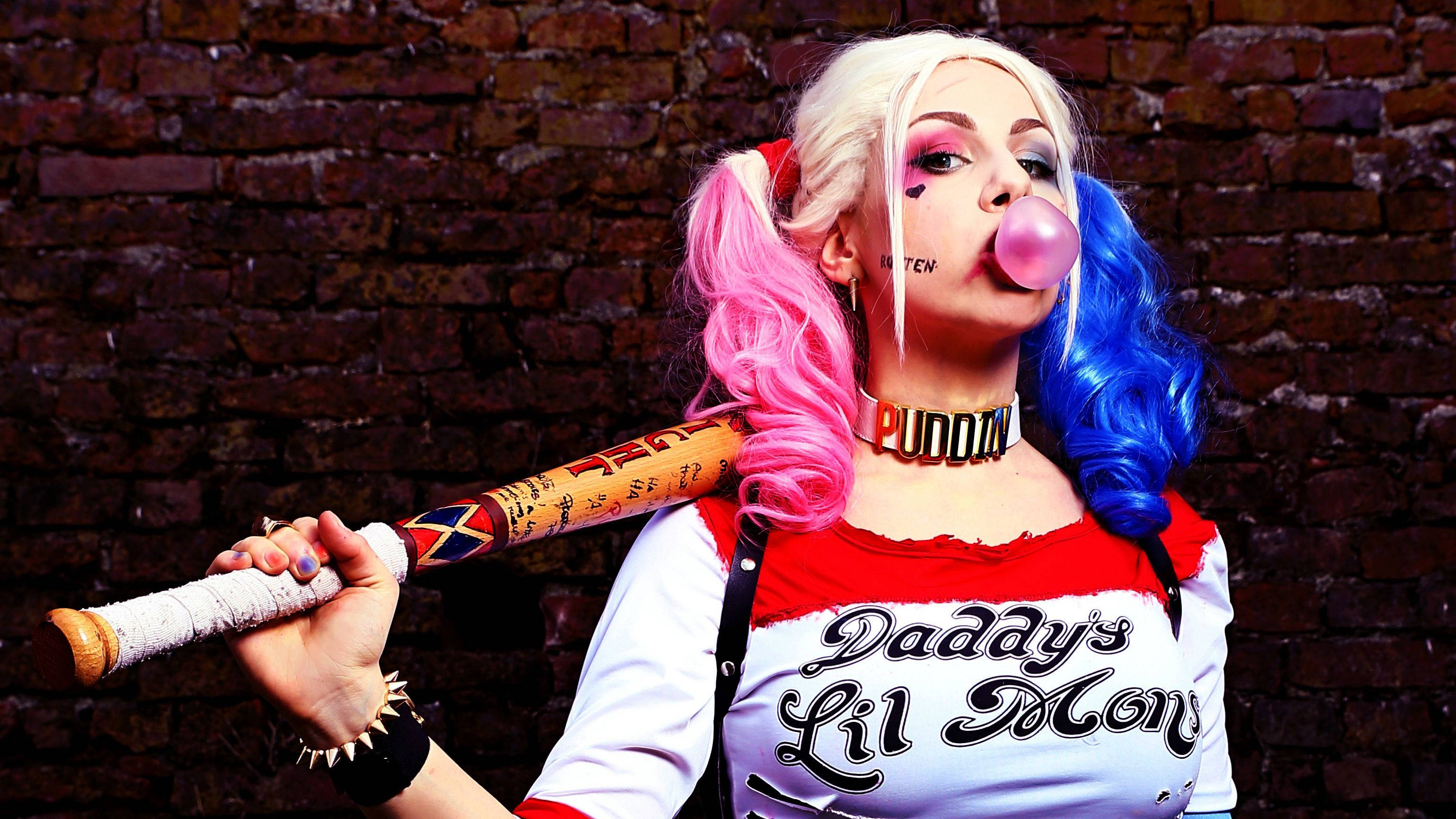 Harley 桌布 壁紙 — 一個扮成哈莉·奎茵的人，拿著棒球棍靠著磚牆吹泡泡糖。
